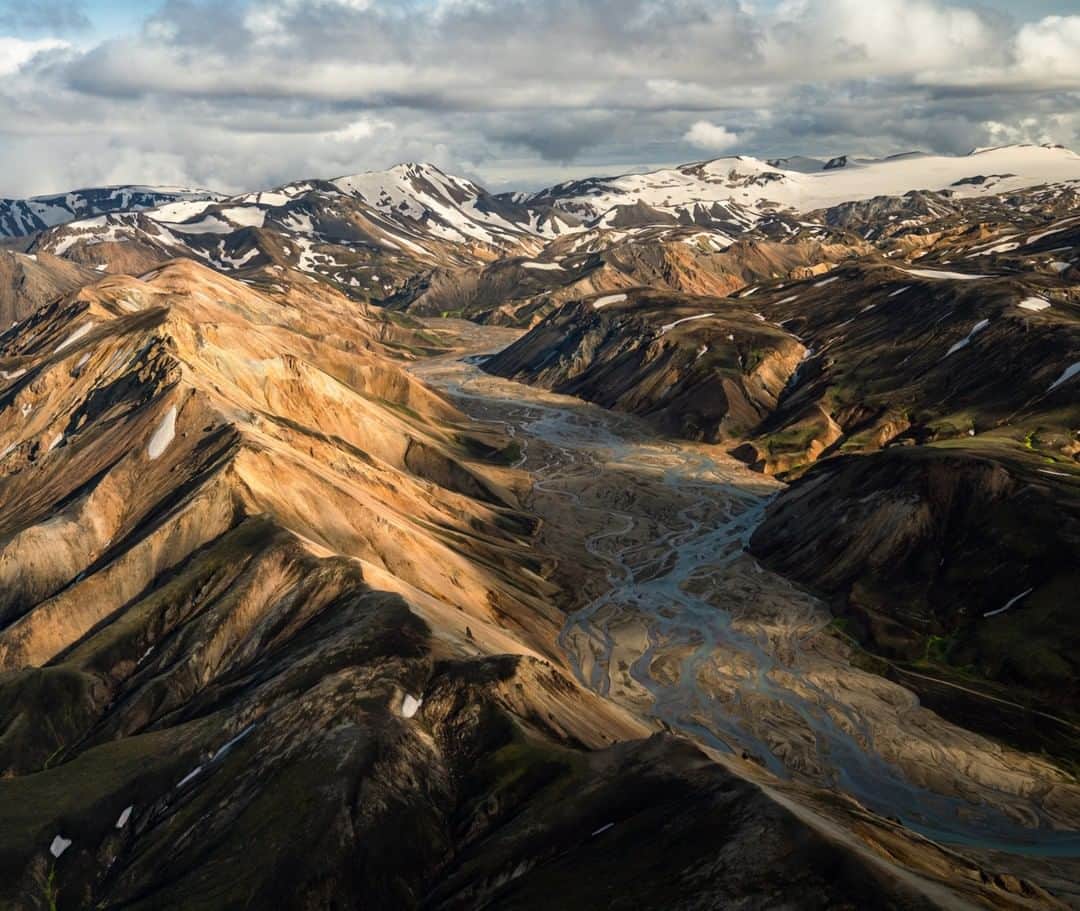 National Geographic Travelさんのインスタグラム写真 - (National Geographic TravelInstagram)「Photo by @chrisburkard | Unearthly and isolated, Landmannalaugar is in the highlands of Iceland. Warm summer air causes glacial snowmelt to run through the valley, forming these incredible braided rivers. The mineral-colored slopes contrast with the obsidian lava fields with white snow dividing small ridges, giving it this abstract appeal.」3月26日 5時06分 - natgeotravel