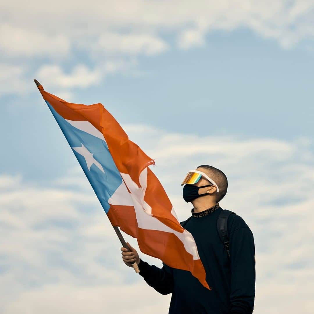 TIME Magazineさんのインスタグラム写真 - (TIME MagazineInstagram)「@badbunnypr, photographed waving a Puerto Rican flag on July 17, joined protesters who gathered outside the Capitol Building in San Juan, #PuertoRico, as calls grew louder for Governor Ricardo Rosselló's resignation in the wake of "chatgate." The trap artist, who encouraged Puerto Ricans to take to the streets on Wednesday, said on Instagram he was postponing part of a European tour to join them in demanding #rickyrenuncia. The 25-year-old—real name Benito Antonio Martínez Ocasio—was among several entertainers who showed up to support the demonstrators, including rapper René Pérez Joglar (@residente) and singer @ricky_martin, who was mocked in the chats. #BadBunny said he hoped even those who had never taken part in a #protest would pour onto the streets, without fear. Photograph by @cgregoryphoto for TIME」7月18日 14時01分 - time