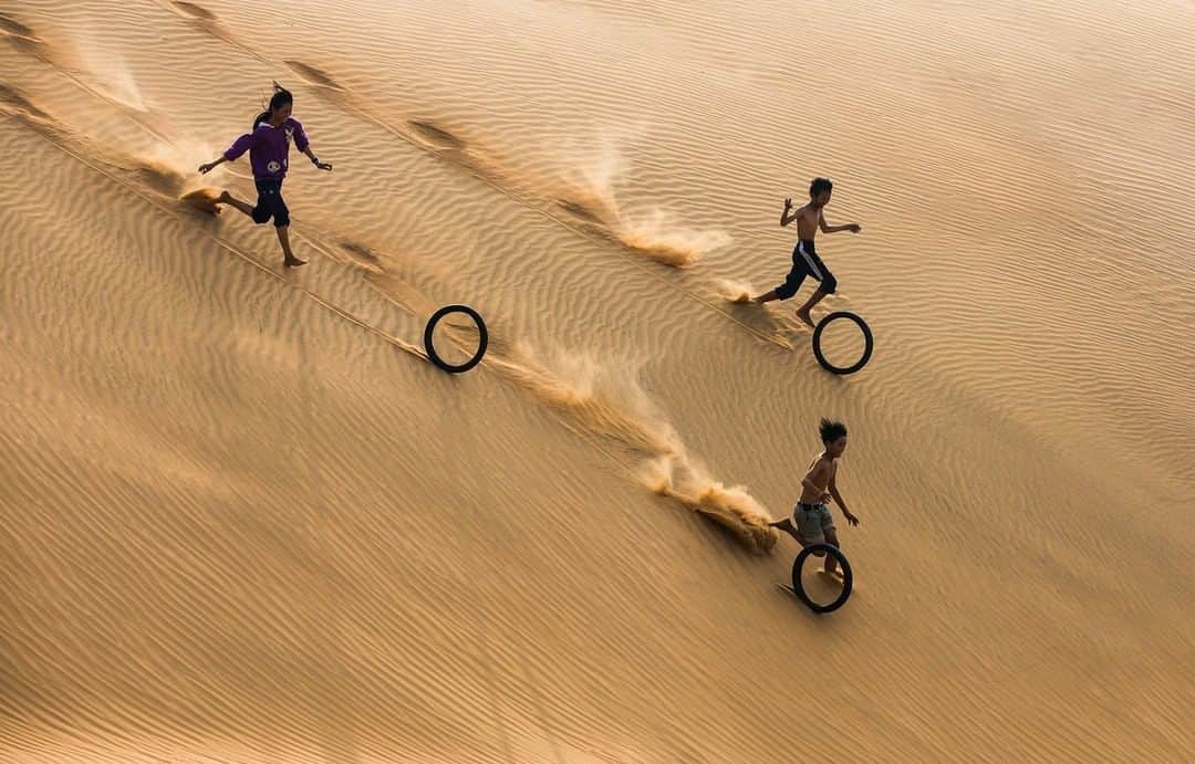 Canon Asiaのインスタグラム：「“A group of children laugh as they play with old motorbike tires on a sand dune near the beach of Mui Ne, a coastal fishing town in the Binh Thuan province of Vietnam. This simple game is played by children all over the world.” • The carefree joy of child’s play 🚲 is always an uplifting sight! Master the use of negative space to create a sense of movement and speed ⚡ just like @vietsui did. Notice how the three subjects are also arranged to create a subtle triangular composition? This results in a harmonious, well-balanced image. Try it for yourself; apply the theory of the golden triangle 📐 to enhance your next shot! • 📷 Image by @vietsui shot using the Canon EOS 5D Mark III | Canon EF 70-200mm f/2.8L IS II USM Lens | f/7.1 | 1/800s | ISO 200 | 130mm  Want your photos to be featured too? Tag them with #canonasia or submit them on My Canon Story, link in bio!  #canonasia #photography #muinevietnam #vietnam #vietnamphoto #vietnamphotography #sand #sanddunes #negativespace」