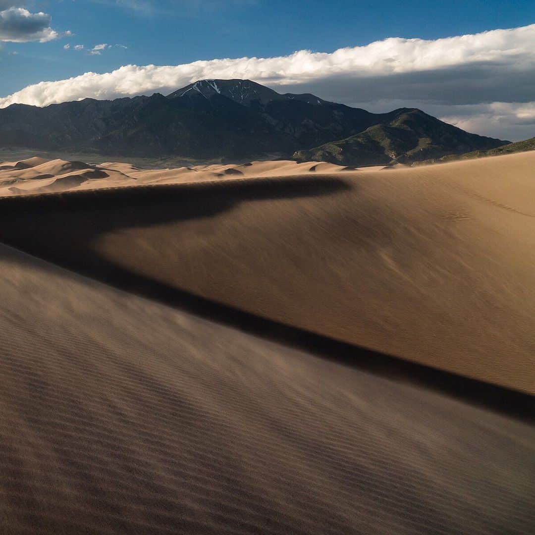 National Geographic Travelさんのインスタグラム写真 - (National Geographic TravelInstagram)「Photo by @stephen_matera | Wind blown sand across Great Sand Dunes National Park at sunset, Colorado. The area receives only 11 inches of precipitation each year and was measured to be the quietest of the U.S. National Parks in the contiguous 48 states. The park also contains the Sangre de Cristo Mountains with six peaks over 13,000 feet. Sand temperatures can reach a blistering 140 degrees Fahrenheit during hot summer days and dunes are up to 750 feet high. Follow me @stephen_matera to see a video of the sand blowing and for more images like this from the Colorado and around the world. #desert #sangredecristomountains #colorado」7月20日 7時01分 - natgeotravel