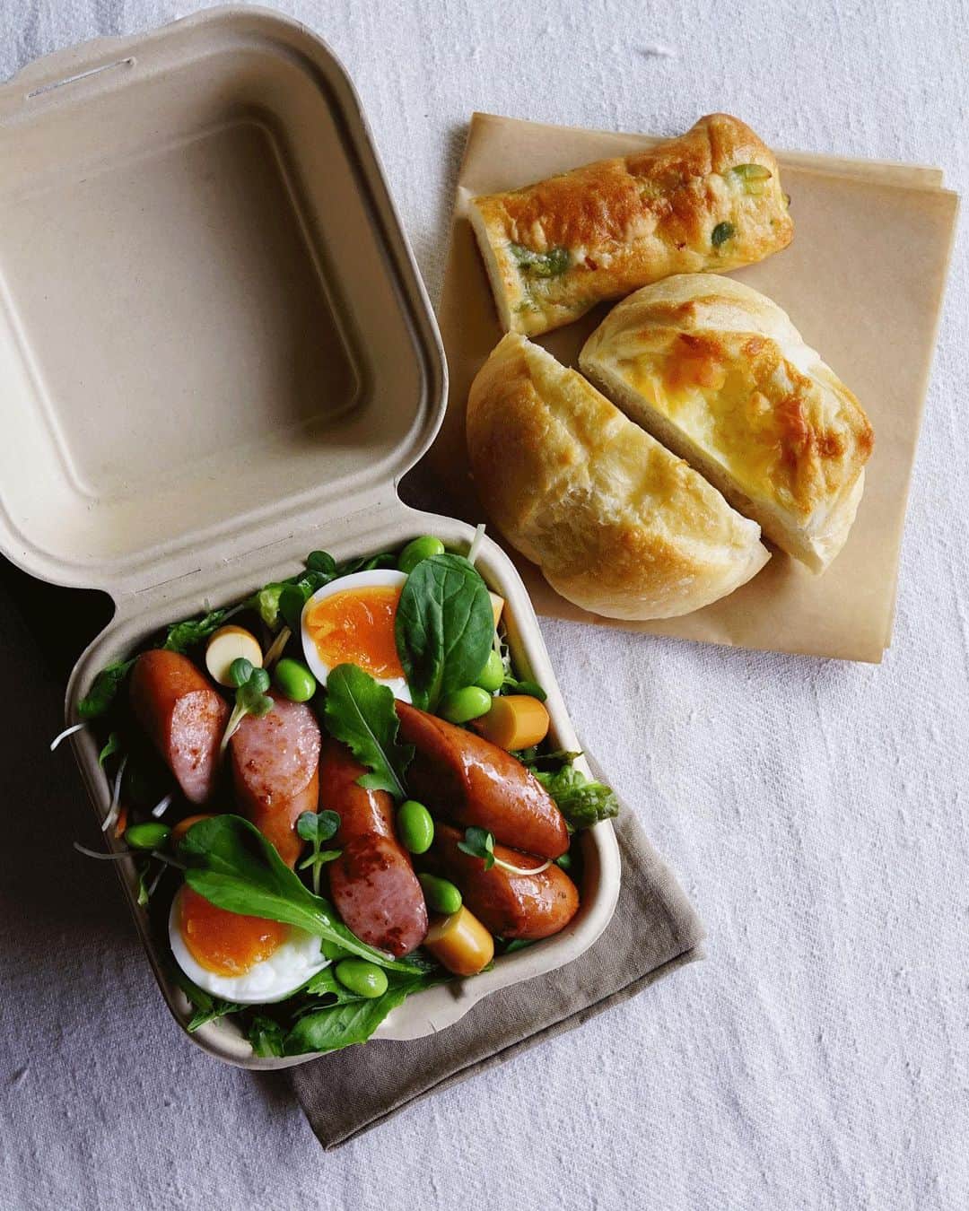Ryoko Yunokiのインスタグラム：「+ + + Bread and salad bento/パンとサラダのお弁当 . *some bread *Green salad, topped with stir-fried sausage, baby tomatoes, smoked cheese, and green olives, seasoned with salt/pepper and drizzled olive oil . *パン *グリーンサラダ。ソーセージの炒め物、プチトマト、スモークチーズ、グリーンオリーブ。味付けは塩胡椒とオリーブオイル + + + #bento #お弁当 #丸の内弁当 #f52grams #紙パック弁当」