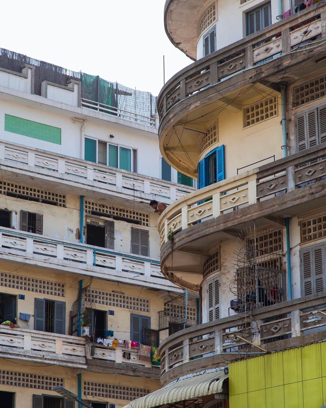 Shunsuke Miyatakeのインスタグラム：「A man at the classic balcony.  There are several classic buildings in the middle of Phnom Penh. At a glance, they seem to be dirty and uncomfortable from outside, but some are getting renovated and so cozy inside with reasonable price. They are people welcome houses. I feel classic Cambodians used to live like that, and the people who see the value in experiences or time with friends would love them.  Nowadays, modern apartments and condos are built rapidly here and there in this town. Most of them look beautiful from outside, but they are in the same format, and so boring with tiny balcony and unreasonable price. They are people unwelcome houses. I feel no uniqueness and only the people who see the value in things would like them.  Of course, I love this man enjoying his time at his balcony.」