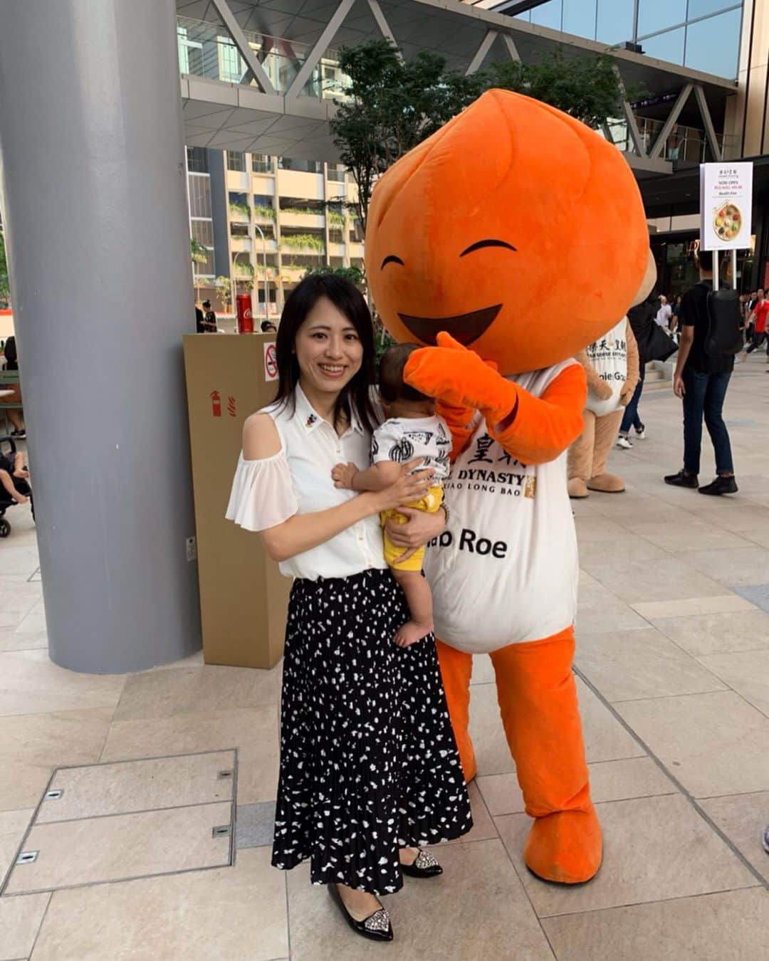 大西蘭のインスタグラム：「・ オープンしたばかりのPaya Lebar Quarter ✨ ・ 広場にいたこのキャラクターは何？と思って近づいてみると🧐 ・ 小籠包⁉️😂 ・ ８色小籠包が有名なParadise Dynastyのプロモーションでした！ ・ このオレンジの小籠包くんはcrab roe小籠包🦀 ・ 他の色の小籠包たちもいましたよ😊 ・ こぐまちゃんは小籠包くんに釘付けでした🙄 ・ 頭の感じが似てるからかな？😂 ・ ちなみにこの８色小籠包は銀座でも食べられますよ😋 ・ モールはまだオープンしていない店舗も多く、レストランはどこも混み合っていて、並ぶのも大変なので、フードコートでサクッと食べました😋 ・ この麺が結構美味しかった🍜 ・ ミルクティーのカップのイラストのおじさん？お兄さん？がレトロ可愛い😂💕 ・ 私の着ている服はよく見ると、襟にミッキーミニーが付いています💕 ・ 👚 @lzzieofficiel ・ 👠 @elisalitz ・ ・ #paradisedynasty  #xiaolongbao #crabroexiaolongbao  #payalebarquarter」