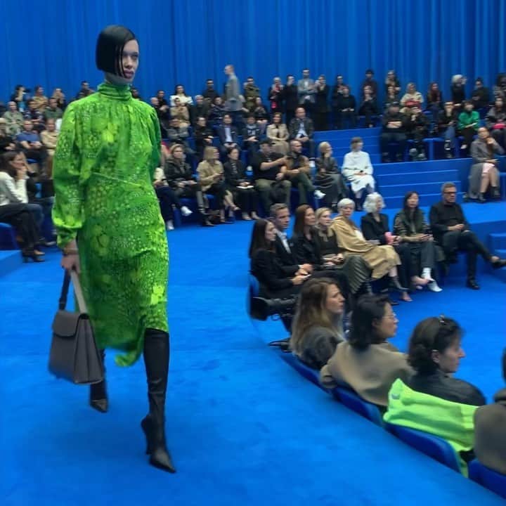 のインスタグラム：「欧州議会のような青いすり鉢状の会場。緩やかなスロープを闊歩するのは、幅広い年代の現代人。「あらゆる職業のパワードレッシング」やユニフォームをテーマに数々のシルエットに挑戦した。流れるようなカットのドレスでも、シームをツイストするなどのギミックを効かせるこだわりはデムナならでは。頬骨を尖らせた「パワーチークボーン」や、一部のモデルに施されたヒアルロン酸を注入したような口もとの特殊メイクアップは、シニカルな演出か。 ニュース番組のアンカーウーマンを思わせるプリントや、幅広いプリーツを施したドレス、上下で取り外しができるチェーン柄のドレスや、シームを一切配したタキシードルック、デニムに見えるようで実はサテンにジーンズのプリントがなされたセットアップなどひねり技が光る。ラストの砂時計型のドレスシリーズは、クリノリンを取り外せばボリュームダウンしたシルエットが楽しめる仕掛け。 恒例のストリートキャスティングで見出された個性あふれるモデルたちも圧倒的な存在感。プロでは、往年のスーパーモデル、ナジャ・アウアマンの久々のウォーキングが話題を呼んだ。#balenciaga #spur #pfw20ss #thebestrunways2020ss #spur編集G @balenciaga」
