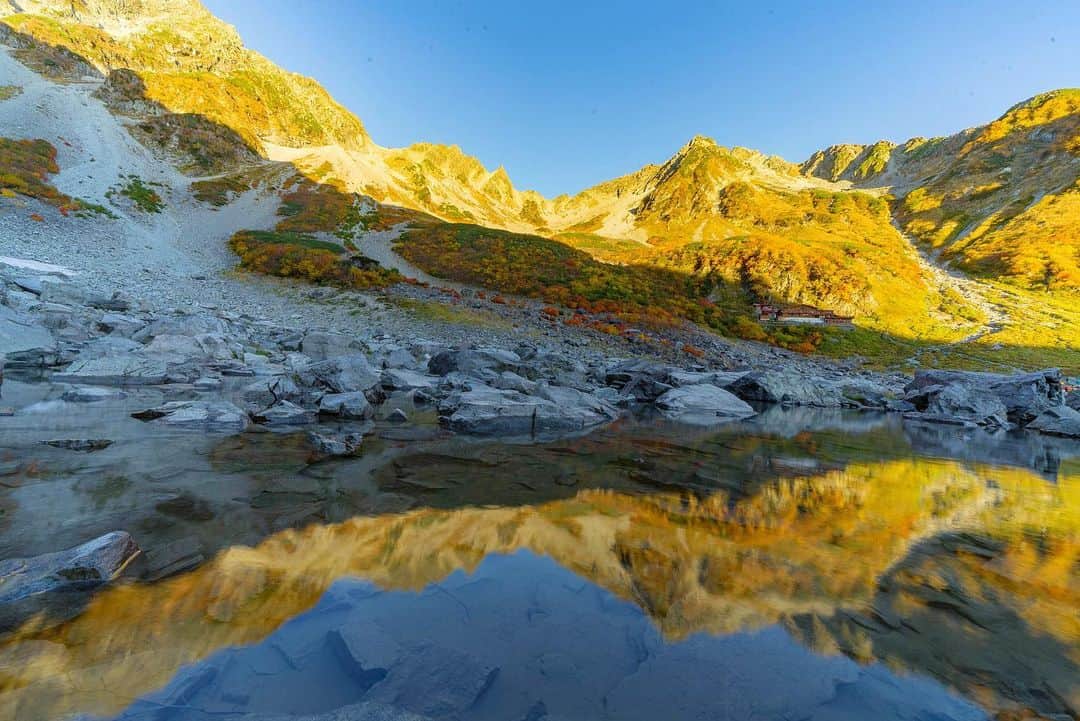 詩歩さんのインスタグラム写真 - (詩歩Instagram)「🍁﻿ ﻿ 鏡面反射する秋色の山⛰﻿ Beautiful reflection of autumn-colored mountains.🍁﻿ ﻿ 山の朝は早い！﻿ 日の出より早く起きて、日の出の瞬間を狙います。﻿ ﻿ といっても、ここ涸沢カールは標高の高い山に囲まれてるので、地平線からの日の出を見るのではなく、朝日に照らされる山の稜線(モルゲンロート)をみます😊🌅﻿ ﻿ この写真は、早起きしてモルゲンロートを見た少し後の写真📸﻿ ﻿ 涸沢ヒュッテの横にある”池” まで歩いていくと、山が鏡のように美しくリフレクションする様子が見られます😍﻿ ﻿ が、かなり寒いので池は一部すでに凍ってました🥶❄️﻿ そりゃ寒いわけだ。。笑﻿ ﻿ ﻿ まだまだ涸沢の写真あげてくのでお付き合いください🙇‍♂️﻿ ﻿ ﻿ 📷9th Oct 2019﻿ 📍涸沢カール／長野県　﻿ 📍Karasawa Cirque／Nagano Japan﻿ ﻿ ﻿ 台風19号被害で被災された方に、１日でも早く平穏な時間が訪れますように。﻿ ﻿ ﻿ ©Shiho/詩歩」10月14日 13時22分 - shiho_zekkei