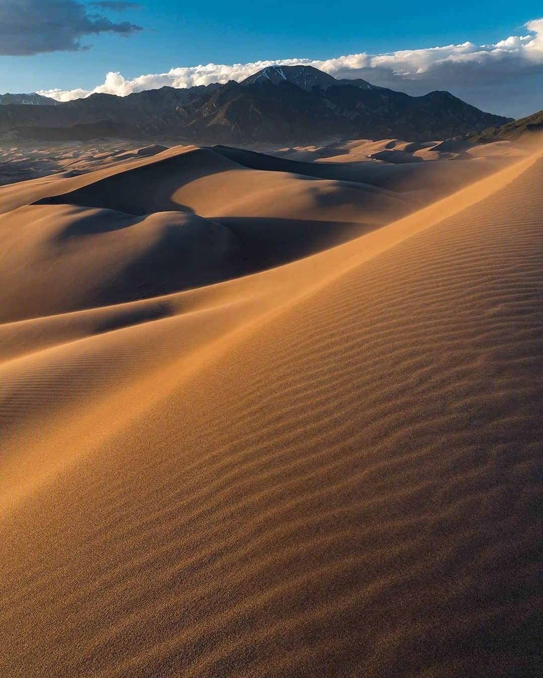 National Geographic Travelさんのインスタグラム写真 - (National Geographic TravelInstagram)「Photo by @stephen_matera | Windblown sand covers Great Sand Dunes National Park at sunset in Colorado. The area receives only 11 inches of precipitation each year and is the quietest U.S. national park in the 48 contiguous states. Sand temperatures can reach a blistering 140°F during hot summer days, and the dunes are up to 750 feet high. The park also contains the Sangre de Cristo Mountains, with six peaks over 13,000 feet.  Follow me @stephen_matera for more images like this from Colorado and around the world. #desert #sangredecristomountains #colorado」10月30日 9時04分 - natgeotravel