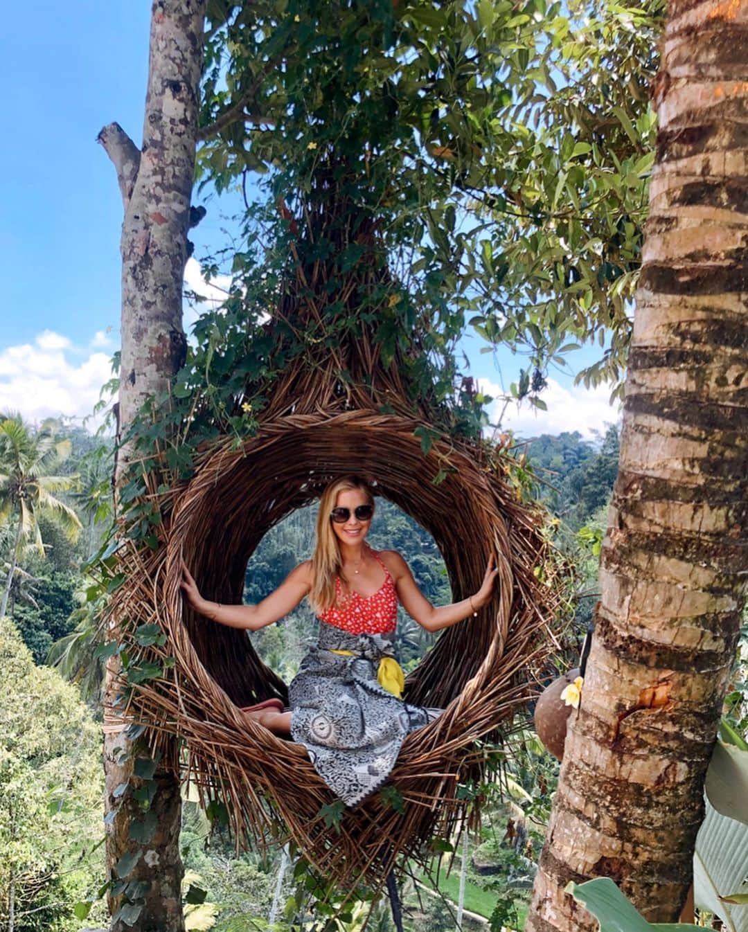 のインスタグラム：「Finally getting around to posting from the trip we took a little bit ago. We went to Bali and I can’t wait to share some of our adventures with you! 🌴🌱🌿 Try to overlook my very forced and scared smile as I was way too high off the ground for my own comfort! I was also wondering if the nice Balinese men that were taking my picture knew if their nest (a handful of roots hanging from a palm tree 1000 feet in the air) was definitely a secure construction. #bali #ubud #traveltheworld #balivacation」