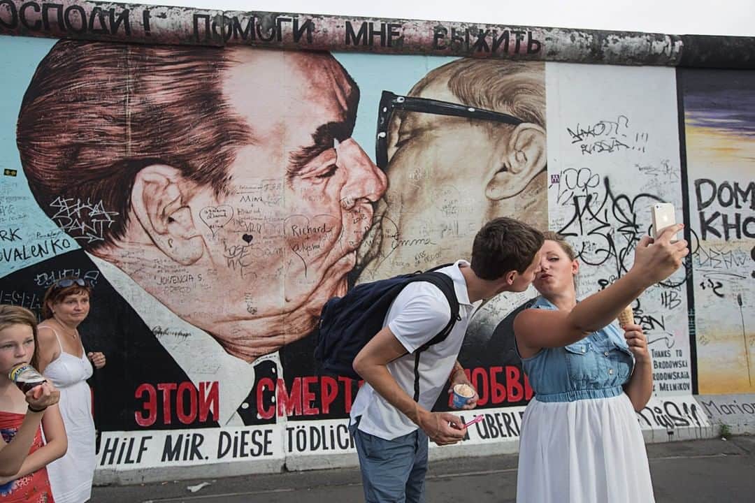 ナショナルジオグラフィックさんのインスタグラム写真 - (ナショナルジオグラフィックInstagram)「Photo by @gerdludwig | A couple takes a selfie in front of the most famous mural on the Berlin Wall, called "The Kiss of Death" by artist Dmitri Vrubel, which depicts the late Soviet premier Leonid Brezhnev kissing his East German counterpart, Erich Honecker.  November 9 marks the 30th anniversary of the fall of the 96-mile-long Berlin Wall, which physically divided East and West Berlin from 1969 to 1989.  The East Side Gallery, a 1.3-kilometer-long section of wall that once circled West Berlin, is now an international memorial to freedom. The paintings document a time of change and express hopes for a better, more open future for the entire world. @natgeoimagecollection @thephotosociety #BerlinWall #Berlin #Germany」11月10日 1時35分 - natgeo