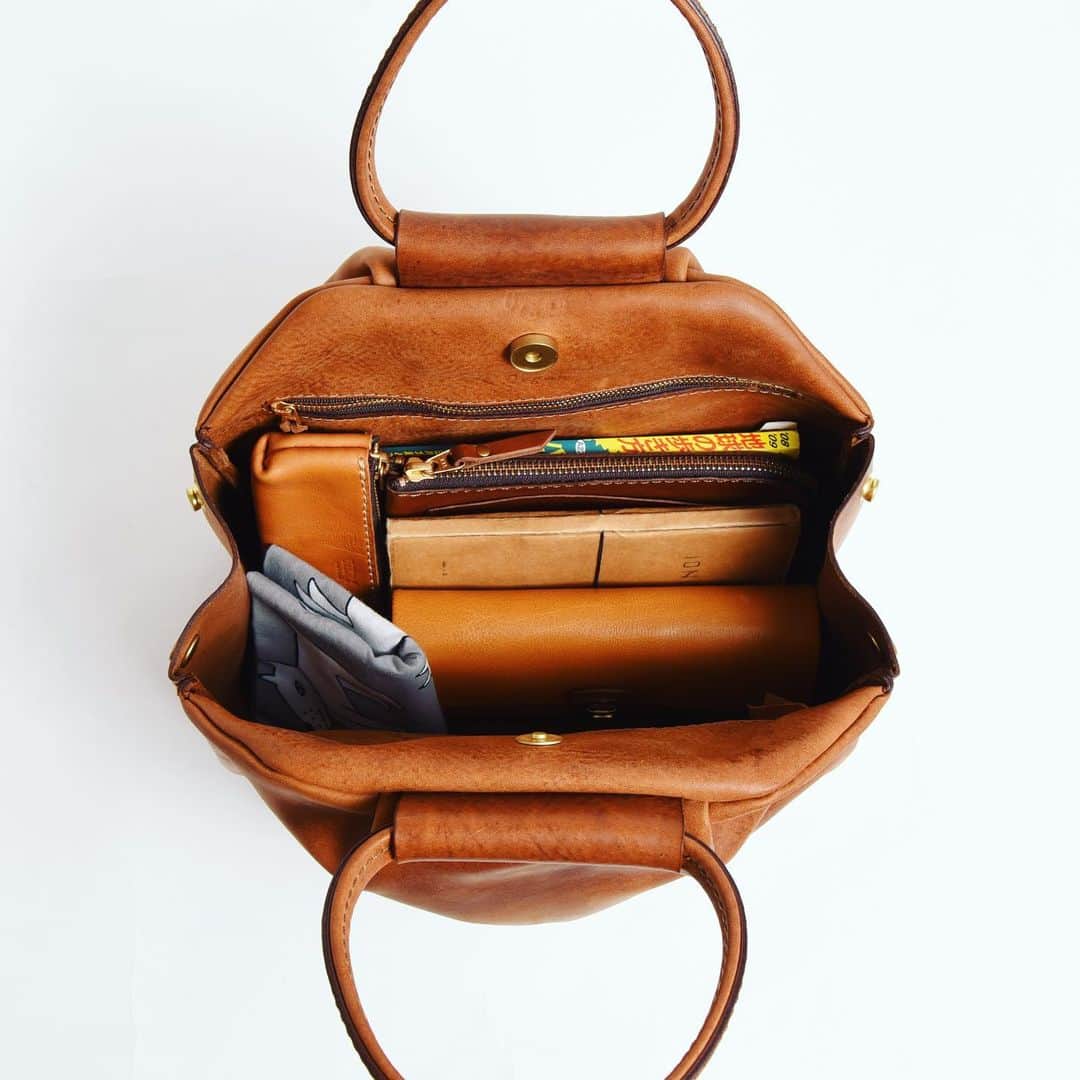 HERZ ヘルツさんのインスタグラム写真 - (HERZ ヘルツInstagram)「#旅モノ 2019﻿ オンラインショップ販売アイテムをピックアップ！﻿ ﻿ 【タックハンドバッグ(TB-1928)】﻿ @organ_leather の作り手による、旅先にも普段使いにもおすすめのハンドバッグ。﻿ 実はこの鞄。旅モノ販売前にスタッフ内でお披露目会をした時に一番人気のあったものです。﻿ ﻿ 商品名の通り、作り手が拘ったのは、タックの作り。﻿ 本体前後面合わせて8カ所にタックを作り、ぽってりとしたフォルムにしています。﻿ ﻿ 鞄本体の雰囲気と一体感を出すために取っ手も丸い形に。﻿ 全体を通してステッチが目立ちにくい作りにしており、スッキリとした見た目にしています。﻿ マチ上部のホックを外せば、収納部がガバっと開き、容量もアップします。﻿ 内側前後面にあるポケットは女性に嬉しいファスナー式。﻿ タックを入れた分、ポケット自体の容量も多く、沢山収納できるところも使い勝手に貢献しています。﻿ ﻿ 革はOrganで使用している #イタリアンレザー の #ミッスーリ を使用。﻿ あまり可愛くなり過ぎないように、表情が強めのミッスーリで作りました。﻿ ﻿ #ヘルツ #organ #organbag #ハンドバッグ #レディースバッグ #旅行鞄 #作り手 #革職人 #旅行鞄 #革 #イタリア革 #革鞄 #革製品 #革小物 #herz #herzbag #leather #bag #leatherbag #leathergoods #handbag #ladiesbag #madeinjapan #factory」11月20日 11時23分 - herz_bag