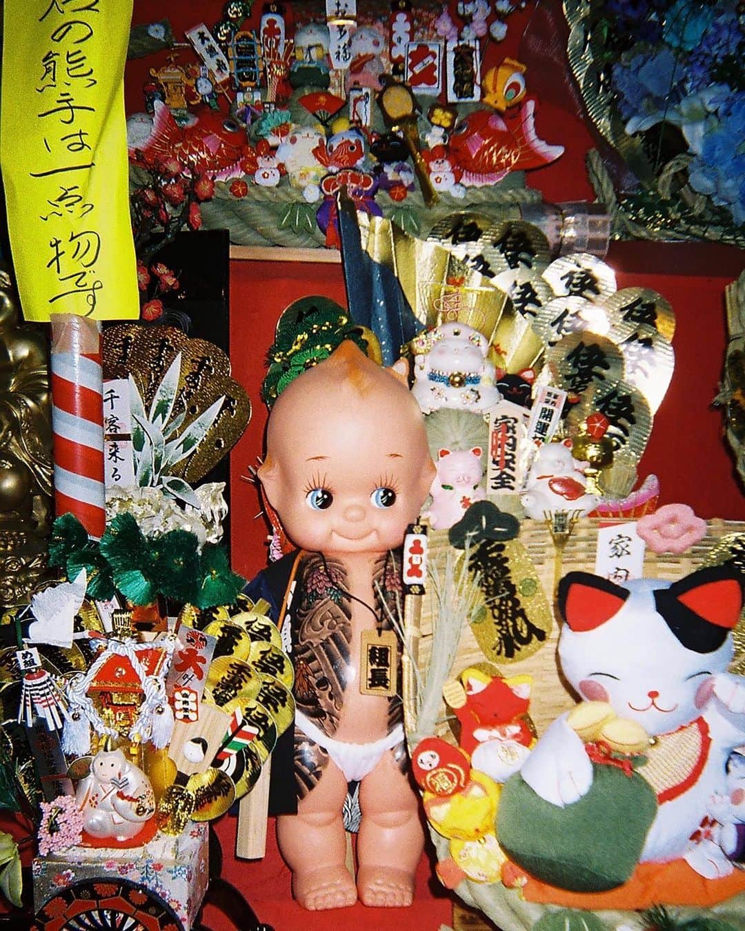 東京DANDYのインスタグラム：「You know the year's coming to an end when you see photos from the Toro-No-Ichi festival at Hanazono Shrine. The exact origins of the 300-year-old tradition are unclear, but it's believed that at an Edo Period farmer's market, lucky coins and trinkets were attached to tools to bring luck. This has evolved over the years into today's extravaganza where ‘kumade,' bamboo rakes for individuals and businesses to 'rake in' good luck and money, are blinged out to the kitschy Japanese max. People of all ages and backgrounds participate, including the local yakuza (as celebrated in this tattooed kewpie doll.) Photo from DISPOSABLES book, link in bio. . #DisposablesBook #Disposables #花園神社 #Festival #Yakuza #Tattoo #入れ墨 #35mm #Shinjuku #Tokyo #使い捨てカメラ #酉の市 #祭り」