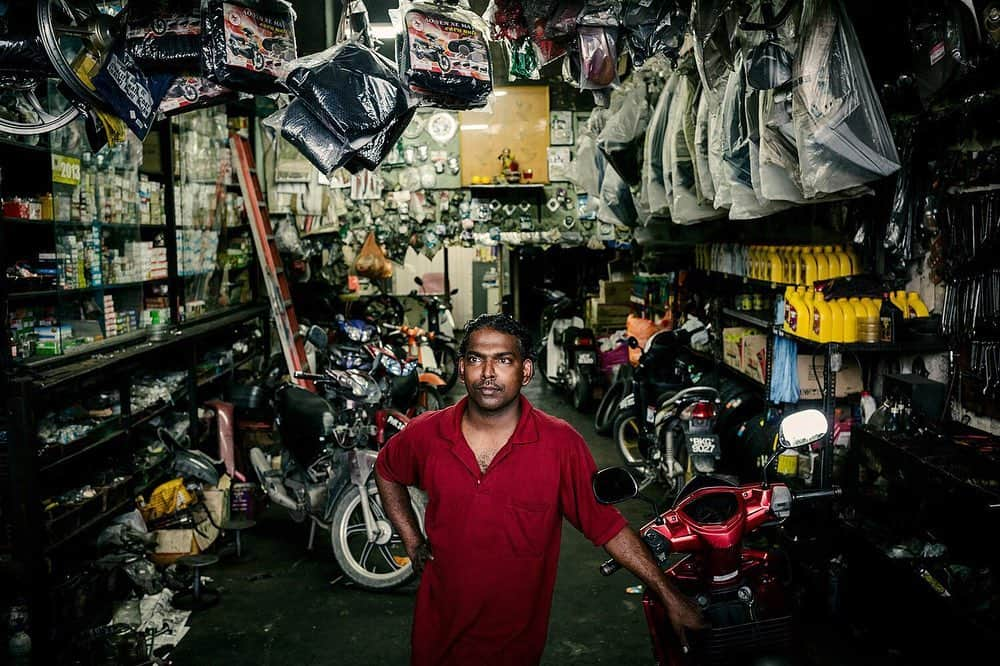 ナショナルジオグラフィックさんのインスタグラム写真 - (ナショナルジオグラフィックInstagram)「Photo by @iantehphotography | Ramesh, a mechanic at Gopal Motors, Port Klang. I spent several days photographing around this dilapidated colonial building near Malaysia’s largest port. A major highway was built from the loading docks, bypassing this little town, with busy roads and flyovers splitting into two levels before swooping past (a few feet away) the windows and doorways of the building. The loud and heavy traffic of container trucks trundling by over the years has literally squeezed the life out of this once beautiful and historic building, now only a flicker of its former self. Only this  mechanic’s garage—where I met Gopal, working late into the night servicing scooters—seemed to be doing quite well. When I left to go back to my car, I passed empty shop lots, a run-down cafe with barely a customer, followed by more boarded-up shop fronts, and finally a brothel, its dark entrance next to the charred remains of a store. As I look up at the gaping roof, I see the sky and the roots of a banyan tree growing along the walls of its crumbling interior. #malaysia #banyan #dereliction」12月14日 0時37分 - natgeo