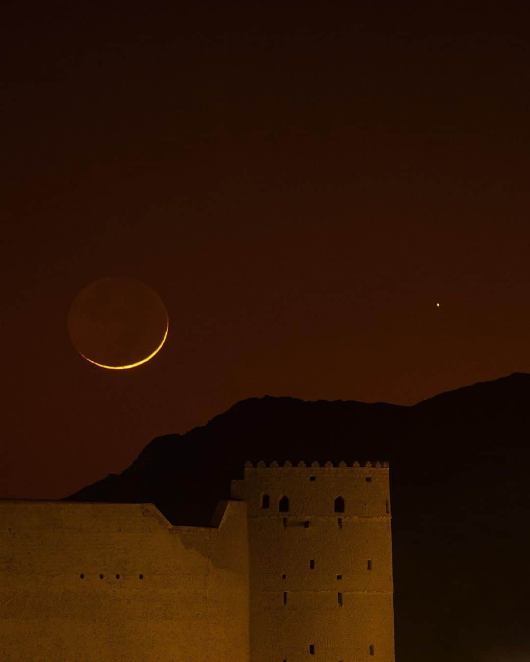 National Geographic Travelさんのインスタグラム写真 - (National Geographic TravelInstagram)「Photos by @BabakTafreshi | The new moon appears in a colorful dusk over Bahla Fort, a World Heritage site at the foot of the Jebel Akhdar highlands in Oman. Swipe for a closer view of the crescent moon and Saturn in a celestial conjunction, taken on December 27. Built in the Middle Ages, the fortress is one of four located around the town of Bahla.  Explore more World Heritage sites at night @babaktafreshi. #newmoon #middleeast #oman #bahlafort #worldheritage」1月7日 2時07分 - natgeotravel