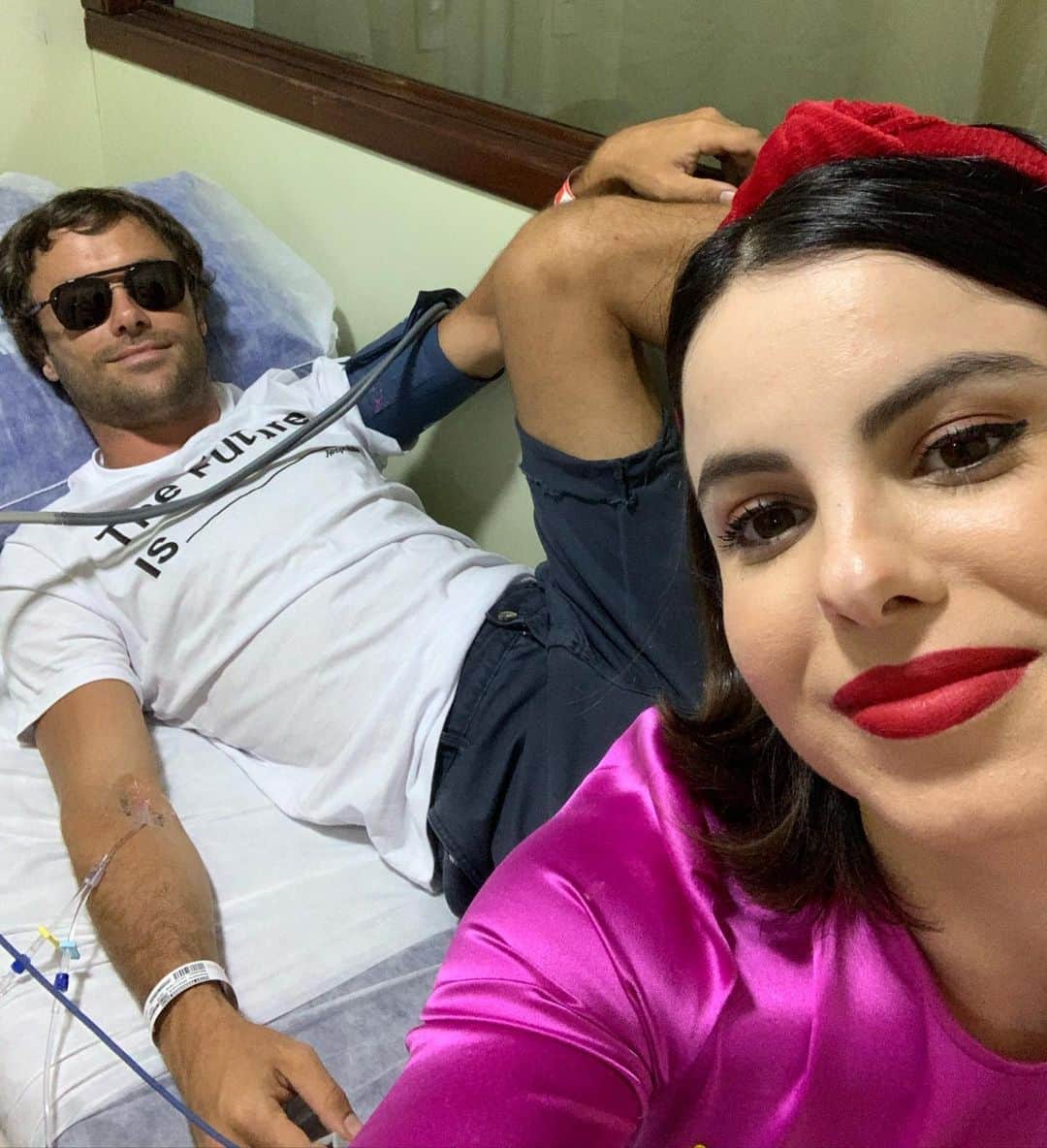 ステファニー・ブリットのインスタグラム：「Com ele é sempre “com emoção”! 😜Cheguei na casa dos meus pais pra passar o Natal, e eis q esse serumaninho não encostava o pé no chão pq o joelho doía mto! Faz o que quando está com mta dor? Remédio né? Ele odeia! Mas nós conseguimos convencer. Ele tomou e dois minutos depois, diz que tá ficando com terçol  pq os olhos estavam ficando inchados! Levei soro pra fazer compressa! Fiquei ali de olho nele e vi uma boca tb inchando. “Kayky vc tá sentindo bem? Sua boca tá ficando inchada!” “To ótimo Thé!” Não acreditei mto! Ele é uma rocha, pra assumir uma dor tem q ser sério mesmo! Fiquei ali quietinha! “Kayky? Tá sentindo alguma coisa na garganta?” “Tá formingando um pouco!” Desci. “Maaaaaae, o Kayky tá tendo uma reação alérgica ao remédio!” Todo mundo sobe! “Kayky, tá se sentindo bem?” Ele responde: “Melhor ir pro hospital!” Correria!!! Lembra q o Kayky não diz nunca  q tá com dor, pedir pra ir por hospital é pq tá mto ruim pra ele! Ajuda o Kayky a descer (não tava encostando o pé no chão, lembra?) Meu pai pega a chave do carro e já entrando no carro lembra q bebeu uma cerveja! “Eu dirijo” gritei! Todos os sinais fechados e eu perguntando de 5 em 5 minutos se ele estava conseguindo respirar e meu pai pedindo pra eu parar de perguntar pra não deixar ele mais agoniado! Chegamos! Kayky desce mancado, e volta mancando! Emergência é na parte de trás. Cadeira de rodas e atendimento! Anti alérgico na veia, tentativa de raiox (não conseguia esticar a perna) do joelho, remédio pra tentar passar a dor e refazer o raiox, óculos escuros e uma acompanhante natalina! 🤙🏼Feliz Natal @kayky.brito na alegria e na alergia Tamo junto pra sempre! ❤️」