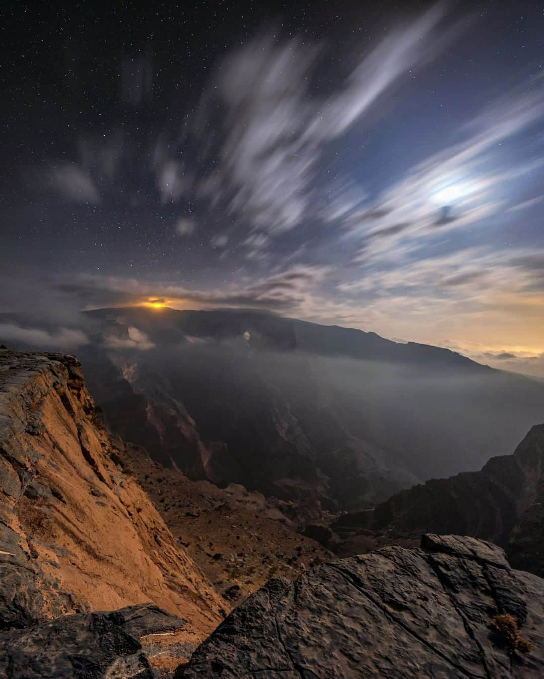 National Geographic Travelさんのインスタグラム写真 - (National Geographic TravelInstagram)「Photo by @babaktafreshi | Standing on the edge of Wadi Ghul, also known as Oman's Grand Canyon. On this winter midnight, the moonlight was gently shining on the massive 1,000-meter-deep (3,200-foot-deep) feature made by erosion. I was near Jebel Shams (Sun Mountain), the highest peak in the country, where you can reach the top of the canyon. The yellow light on the mountaintop comes from the military radar base and observatory on the 3,005-meter (9,800-foot) summit.  Explore more World at Night photography from @babaktafreshi. #nightphotography #oman #jebelshams #canyon」1月31日 10時04分 - natgeotravel