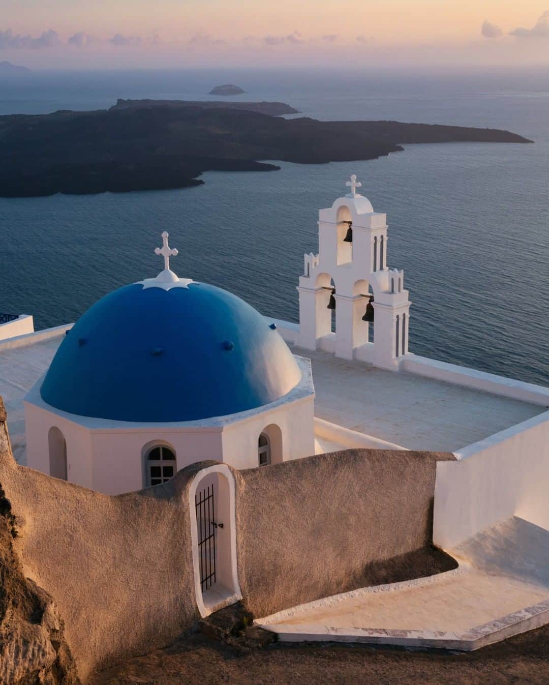 National Geographic Travelさんのインスタグラム写真 - (National Geographic TravelInstagram)「Photo by @MichaelGeorge | This is one of the most photographed spots in Santorini. There are even signs, with this photo, pointing you in the right direction so you can take your own version. I enjoy taking part in the ritual, standing alongside countless others, all pointing cameras in the same direction. My job is normally to break away from the pack and find a unique image or angle. It is an interesting exercise to capture an image that is universally loved and celebrated. It reminds me of a scene from Don DeLillo’s novel “White Noise” on the “most photographed barn in America.” Here is an excerpt: "No one sees the barn," he said finally. A long silence followed. "Once you've seen the signs about the barn, it becomes impossible to see the barn." He fell silent once more. People with cameras left the elevated site, replaced at once by others. “We're not here to capture an image, we're here to maintain one. Every photograph reinforces the aura. Can you feel it, Jack? An accumulation of nameless energies." … “Being here is a kind of spiritual surrender. We see only what the others see. The thousands who were here in the past, those who will come in the future. We've agreed to be part of a collective perception. It literally colors our vision. A religious experience in a way, like all tourism." Another silence ensued. "They are taking pictures of taking pictures," he said. #santorini #greece #travel #natgeotravel #greeksunset」1月11日 6時05分 - natgeotravel