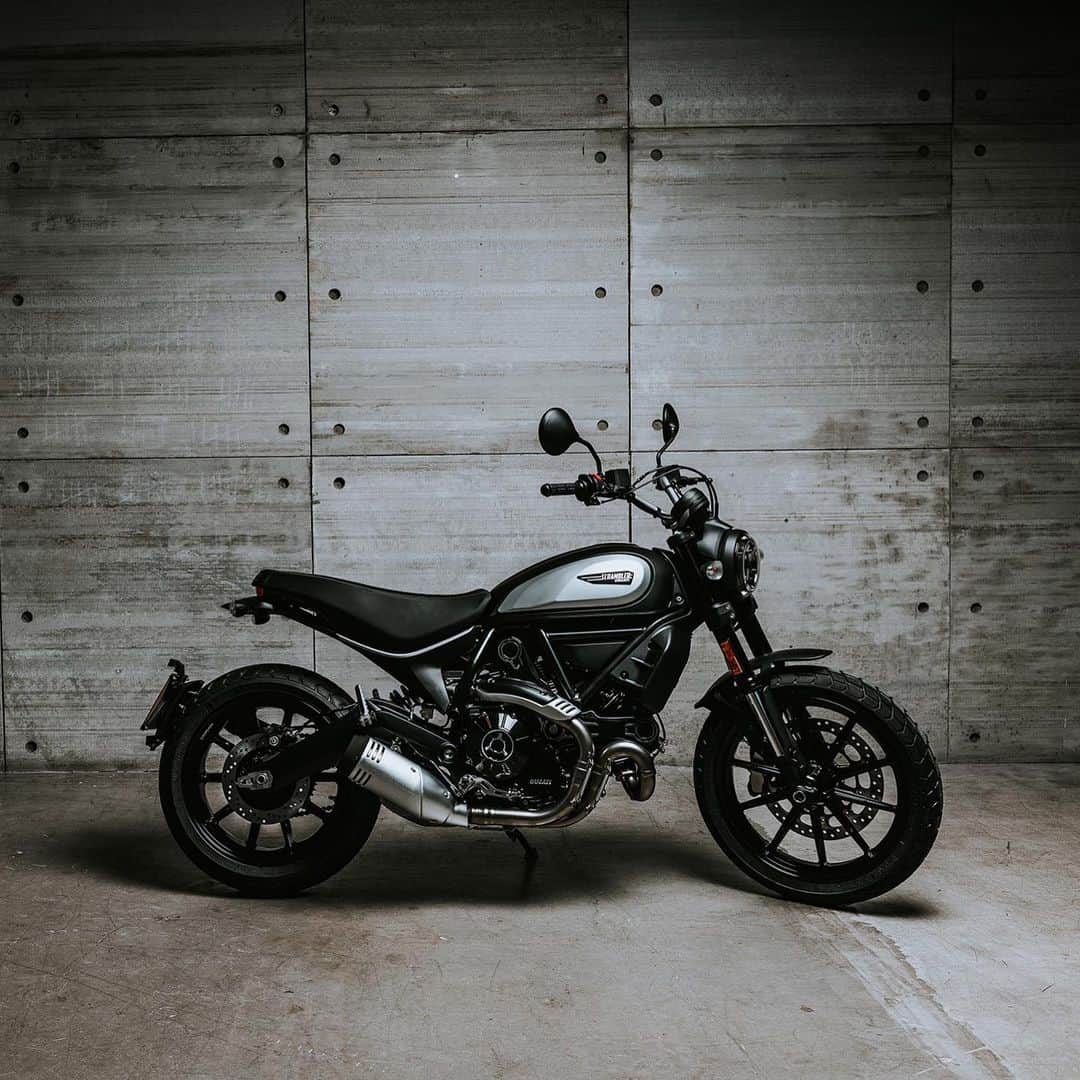 のインスタグラム：「【モーターサイクルショー展示車両紹介/スクランブラー アイコン・ダーク】 ・マットブラックボディ ・ユーロ5適合エンジン ・扱いやすい出力特性  その特徴はマットブラックの燃料タンクとフロントフェンダー。2019年モデルでエンジンはブラックに塗装。クラッチまわりや排気系のカバー類のデザインを変更しました。またホイールはスポーク部分に切削加工を施しました。モデル名通りダークに仕上げたボディカラーによって、スクランブラーのクールな世界を表現しています。  同じく2019年モデルより、エンジンコントロールユニットを見直し扱いやすさを向上。新たに油圧クラッチを採用し、コントロール性も高めています。また前後サスペンションセッティングやライディングポジションも変更。乗り心地はもちろん、オフロードでの走破性も向上させています。スイッチまわりのレイアウトも変更し、操作性もアップしています。見た目は変わりませんが、細かな熟成ポイントを積み重ねることで、そのフィーリングを大きく進化させることができました。  そして排気ガス規制はユーロ4用エンジンと同等のパフォーマンスを備えながら、より厳しいユーロ5規制に適合しています。  スクランブラー ICON Darkは大阪および東京会場に展示予定です。  大阪・東京モーターサイクルショーの出展概要の詳細は @ducatijapan のプロフィール画面のURLからご覧ください。  #大阪モーターサイクルショー2020 #TMCS2020 #ducati #ドゥカティいいじゃん #はじめようバイク」