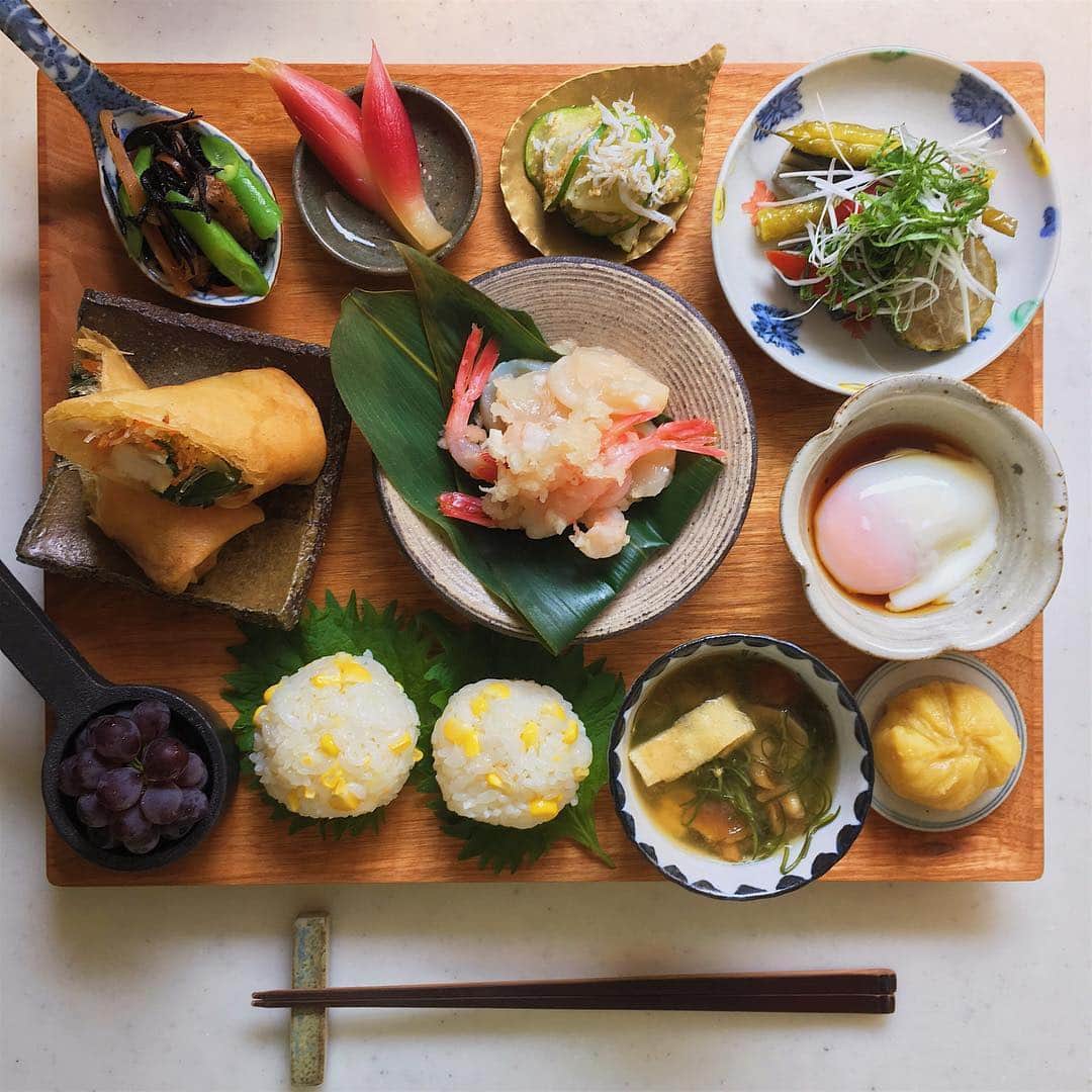 akoのインスタグラム：「Today's breakfast. ワンプレートで朝ごはん 今週もよろしくお願いします☺︎ * ひじき煮 茗荷の甘酢漬け ズッキーニとしらすの胡麻和え 夏野菜の揚げ浸し 春巻き 帆立と甘海老のみぞれ和え 温泉卵 とうもろこしご飯むすび おかひじき なめこ 油揚げの味噌汁 さつまいも茶巾 デラウェア」