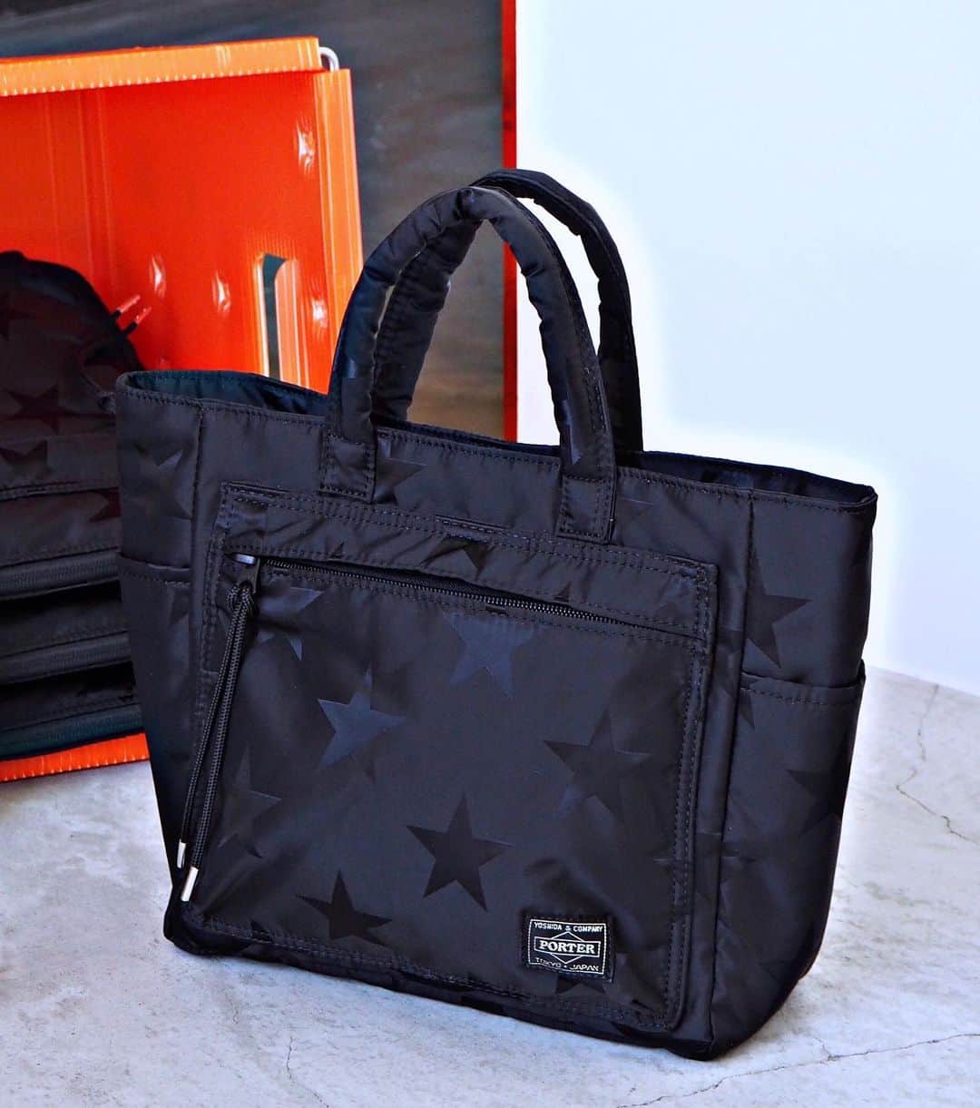 のインスタグラム：「こんにちは。 本日は、PORTER flagship storeにて展開中の「FLAG（フラッグ）」のトートバッグをご紹介いたします。星条旗の星の配列をジャカードに取り入れたシリーズです。高密度に織り上げ光沢感のあるナイロンジャカード生地に綿ボンディング加工を施し、軽さとしなやかさを持つ生地に仕上げました。表面の星柄は、光の角度や見方によって艶やかで立体的な表情に浮かび上がります。ファスナー引手には、シルバーのチップ（アグレット）付きのナイロンコードが付属し、カバン本体のデザインアクセントになっています。  本日ご紹介するトートバッグは、スマートフォンやウォレットなどを収納して、ちょっとした外出におすすめのアイテムです。内装、外装共に、ポケットが充実した機能的な作りになっており、男性女性問わずお使いいただけます。  こちらの商品は、吉田カバン オフィシャルオンラインストアにてご購入いただくことが可能です。 是非この機会にご覧くださいませ。 ※PORTER OMOTESANDO・MARUNOUCHI・OSAKAは当面の間休業となります。何卒ご理解いただきますよう宜しくお願い申し上げます。  フラッグ トートバッグ ￥20,000（税別） size:W350/H370/D130mm https://www.yoshidakaban.com/sp/product/105303.html  #yoshidakaban #porter #luggagelabel #吉田カバン #ポーター #porteryoshida #porterflagshipstore #porterstand #porterexchange #px #kurachikabyporter #potr #madeinjapan #japan #instagood #instalike #instabag #omotesando #marunouchi #osaka #flag #totebag #exclusive」