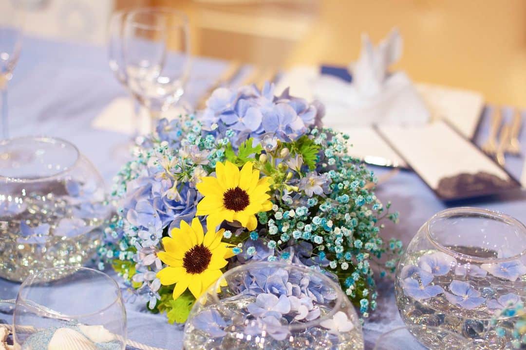 ルミアモーレさんのインスタグラム写真 - (ルミアモーレInstagram)「ブルーのお花の中にひまわりがアクセント . . 夏にぴったりのコーディネートです . . 花びらを浮かべた飾りや貝殻を置くことで更に華やかになりますね . .  オンライン相談会も是非ご参加ください！ ・ https://lumiamore.com/ information_l@lumiamore.com ⠀ ・ ・ 5月6日迄の臨時休業期間中は最小人数で対応しておりますため、お電話が繋がりにくい場合がございます。着信履歴より確認ができましたら折返しのご連絡をさせていただきますが、改めてのご連絡、もしくはメールにてお問合せをいただけますと幸いでございます。 大変ご不便をおかけいたしますが、何卒ご理解賜りますようお願い申し上げます。 ・ ・。・。・。・。・。・。・。・。・。. . 『#lumiamore』のハッシュタグをつけて お写真を投稿してくださいね♪♪. こちらの公式IGで取り上げさせていただきます＊ .  #ルミアモーレ #wedding #instawedding #結婚式 #ウェディング #結婚式場 #f4f #l4l #instagood #プレ花嫁 #結婚式準備 #花嫁準備 #日本中のプレ花嫁さんと繋がりたい #おうち時間 #stayhome #オンライン相談 #オンライン結婚相談 #ブライダルフェア ・。・。・。・。・。・。・。・。」5月1日 19時15分 - baysidewedding_lumiamore
