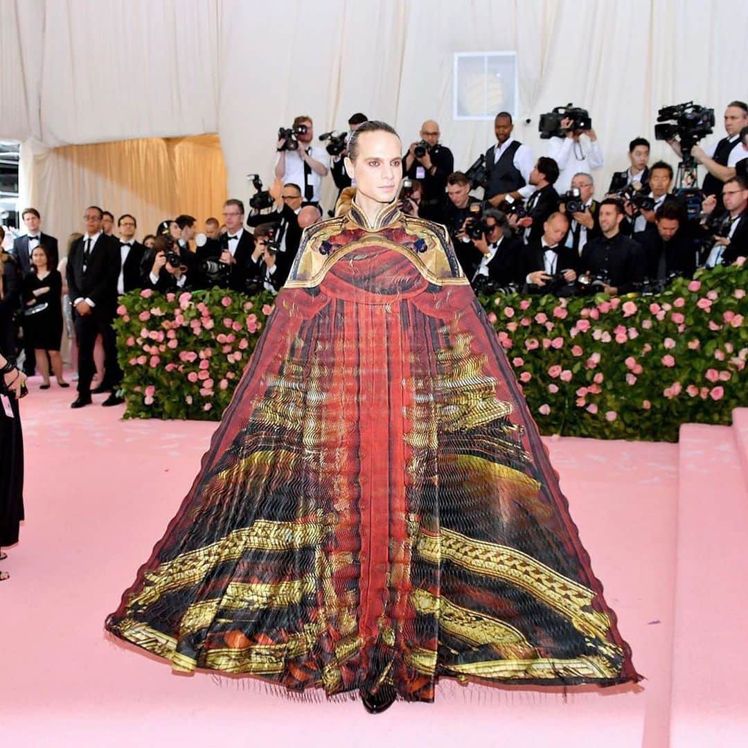 Iris Van Herpeさんのインスタグラム写真 - (Iris Van HerpeInstagram)「The first Monday of May is when the magic of the #Metgala is celebrated. While we look forward to the next gala, we relive last year’s alchemic collaboration with @Jordan_Roth.  To create this look, first, the outer layer was made with the ‘glitch’ delicate laser-cutting technique; each line is 0.8 mm thin, and interlinked to all the other thousands of lines by small waves. The line-design of the waves, when moving, creates a three-dimensional bubble effect and is designed to move faster than the eye can follow - therefore called a ‘glitch’. It literally tricks the eyes and mind. Classical red theatre curtains were printed onto this glitch, and are hanging from the theatre proscenium, which is a cropped tailored jacket. The waves of the red glitch can be compared to a theatre curtain, but instead of revealing the theatre when the curtains are opened, the theatre now lies in between the lines of the fabric and becomes visible when stretched. The ‘glitch' is a technique developed in collaboration with architect and professor @philip.beesley. It uses a hybrid material of cotton and mylar, first digitally printed and then heat-bonded, to finally be laser-cut into a very fine wavy web. A digitally printed silk in a spheroid pattern of 14 meters was placed underneath the ‘glitch’. Finally, a thin boning construction was created to be placed inside, so Jordan is able to extend his arm length. When he unfolds, the cape has a span width of 3.5 meters wide. ~ "As the president of five Broadway theaters, Jordan Roth breathes theatre. We talked about the concept of camp and about exploring the camp of theatre. Part of Jordan’s briefing to me was: 'Put a proscenium around anything, raise a curtain in front of anything, and it becomes performance. Performance is life, framed.’ The look explores the relationship between the fine line of performance and illusion and transforms Jordan into a performance himself.” – Iris van Herpen  Styling: @Michael_Philouze The print of the look features photography by the very talented @Davidleventi Video @Jordan_Roth | @Suzymenkesvogue | @marathondgtl  #irisvanherpen #couture #metgala #jordanroth」5月5日 1時51分 - irisvanherpen