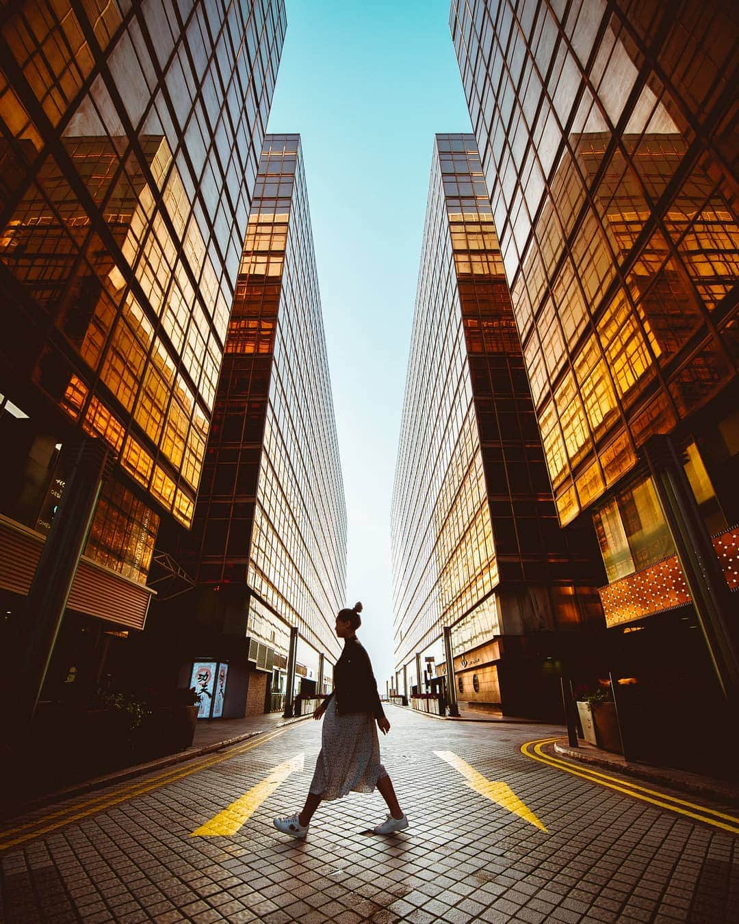 Canon Asiaのインスタグラム：「“The bright sun created strong reflections on the surface of these glass buildings near Hong Kong’s China Ferry Terminal, making the gold pop in beautiful contrast with the clear sky above. I got my friend to stride and underexposed the shot intentionally to capture the blue.” Image captured by @julian_cheong.  Shot on the EOS 5D Mark III with the EF11-24mm f/4L USM at 11mm, ISO 100, f/4, 1/500.  #canonasia」