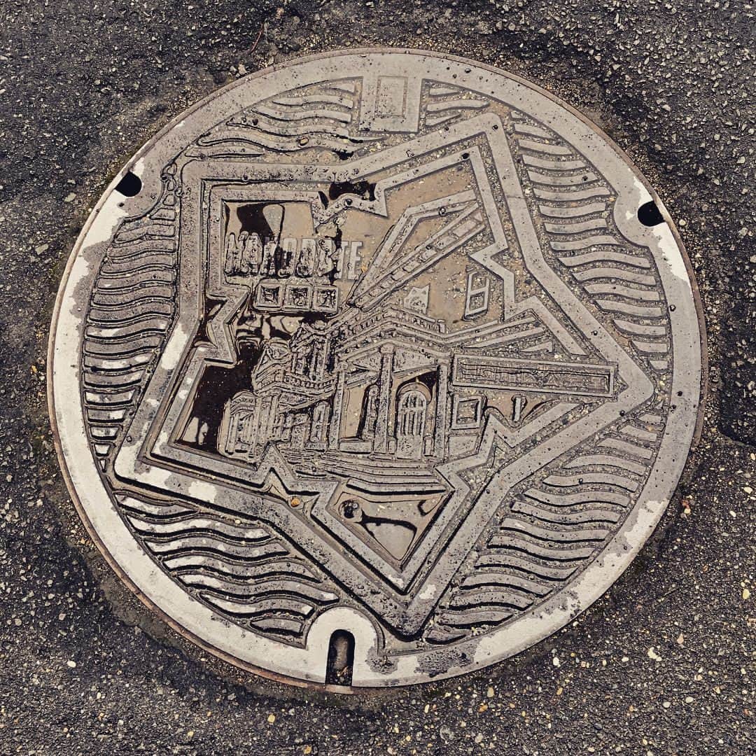 桜井くみ子のインスタグラム：「北海道函館市のデザインマンホール蓋。 ＊五稜郭のお堀 ＊旧函館区公民館(建物名の文字入り) ＊『HAKODATE』『うすい』の文字入り 雨に濡れて、少し分かりにくいですが…国の特別史跡に指定され、日本100名城のひとつにも選定されている『五稜郭』。その星型のお堀の中に、国の重要文化財『旧函館区公民館』がデザインされています！2枚目は、同じデザインで少し小さいサイズのマンホール蓋です！こちらは、建物名は入っておらず、『HAKODATE』と『おすい』の文字入りです。 #デザインマンホール蓋 #函館市」