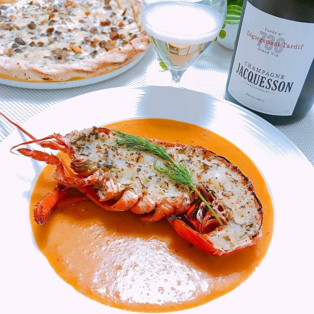 のインスタグラム：「お祝いの食卓に華を添えられて光栄です✨ ご結婚記念日、おめでとうございます！ * #Repost @jpn.buyer • • • 結婚記念日は、少し贅沢に❗️#オマール #アメリケーヌソース #ピザ #ゴルゴンゾーラ #シャンパン #ジャクソン #DT #736 ＊ ＊ オマールエビはピカールで売っていたカナダ産の冷凍。磯の香りや海の塩っぽさが強く、熟成した旨味系のシャンパンにはピッタリの味わい深さでした！ ＊ ＊ アメリケーヌソースの起源は、ネット記事によると下記の通りらしい。 ＊ ＊ 1860年代のフランス。パリにある人気レストラン「ピーターズ」のオーナーシェフであるピエール・フレス氏は、アメリカのレストランで勤務経験がある人物だった。ある日アメリカの観光客が来店した際、店にあったオマールエビを使って即興で作った料理の名前をきかれたピエール氏は、とっさに「オマールエビのアメリカ風です」と答えて大いに喜ばれたのだという。アメリカはオマールエビの一大生産国なので、観光客も嬉しかったのだろう。好評だった料理はそのまま「アメリケーヌ」として定番化した。 ＊ ＊ アメリケーヌを自宅で作るのは手間がかかり過ぎるので、ハインツのビスクスープの袋を買いバターとシャンパンを加えて煮詰め、ソースっぽくトロミと深みを出しました！ ＊ ＊ お料理との相性で分かったのは、熟成シャンパンの濃厚な味わいにはチーズなどのコクが必要ということ。オマールのお料理も、身とソースだけだとシャンパンに負けますが、表面をチーズで焦がした箇所と一緒に食べるとピッタリ。ゴルゴンゾーラとキノコのピザにも相性良く、濃厚さには濃厚さで合わせるのが良いのだと、楽しくも良い勉強になりました！ ＊ ＊ #frenchfood#homard#lobster#sauceamericaine#pizza#gorgonzola#picard#champagne#jacquesson#foodpairing#winelover#おうちごはん#男飯#男料理#フレンチ#チーズ#海老#オマール海老#ロブスター#冷凍食品#ピカール」