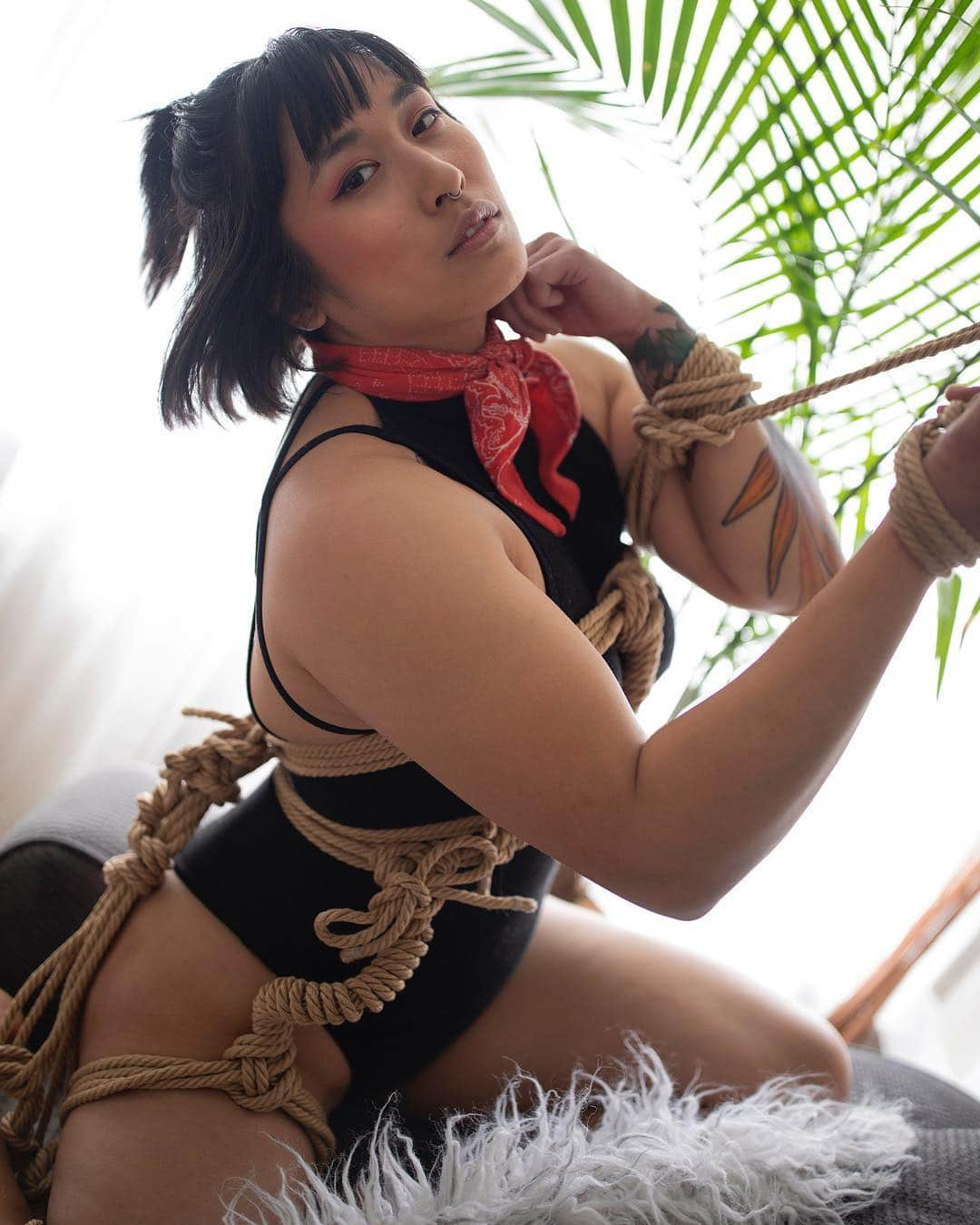 Mia Littleさんのインスタグラム写真 - (Mia LittleInstagram)「Some call me knotty. 📸by @isabeldresler [photo description: Mia is sitting on their knees on a furry draw wearing a black sleeveless bodysuit and red kerchief around their neck. They are tied with rope that is tied to form a hip harness with lovely coiled handles around the hips, a chest harness, a frogged left arm, and cuff around their right wrist. A palms green leaves are in the background]」4月8日 11時56分 - alittleedutainment