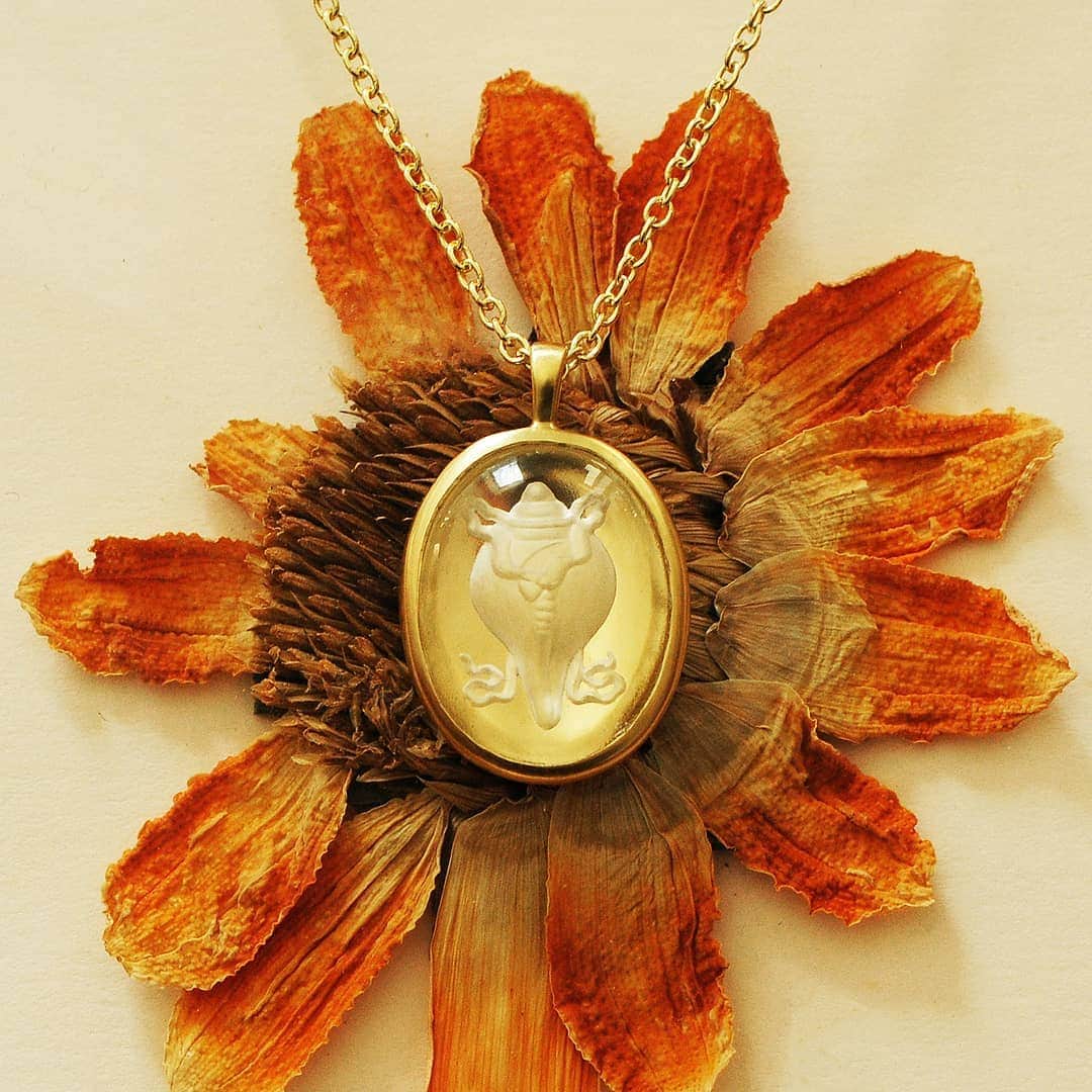 のインスタグラム：「The Right Turning Conch symbolizes the fame of the Buddha's teachings, which spread in all directions like the sounds of the conch trumpet. As one of the oldest ritual objects, it stood for femininity and as a musical offering. Our limited edition rock crystal pendant was hand carved using reverse intaglio, a technique where the shell is carved into the flat back so, that when viewed through the top, the image appears three-dimensional. This limited edition pendant set in 18K recycled gold measures approximately 5/8" in diameter and hangs on a 18" 18K gold chain with a lobster claw closure.」