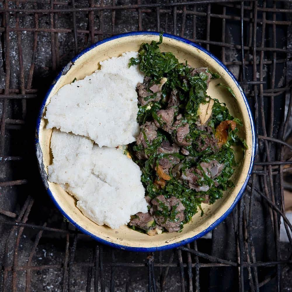 thephotosocietyさんのインスタグラム写真 - (thephotosocietyInstagram)「Photo by @gabrielegalimbertiphoto from his project IN HER KITCHEN / Grandmas always know how to cook! - Normita, 65 – Oltepessi Kenya / Normita lives in a hut made of mud and straws in a masaai village in Kenya. Her kitchen is nothing else than a small cooking area on the ground made of four stones and a metal grill placed on top. Every morning she lights a fire and keeps it on all day long. In her village there are 250 people and more than 500 animals among cows, goats and dogs. She is the chief of the village’s ninth wife and also the oldest woman. Cooking, collecting water from the river and gathering wood for the fire have always been her jobs. She has got 19 grown-up children and more than 40 grandchildren. They all live in the same village / MBOGA AND UGALI: Ingredients: Goat meat and a leg of goat, 50 gr cow’s fat, two tomatoes, 500 gr white corn flour, a plate of sukuma (a vegetable similar to spinach). Ugali is one of the most popular kind of food in Africa. In particular, in this area of Kenya, it is part of the everyday meal and it is at the base of almost any recipe. It is always eaten together with something else: meat, vegetables, fish and so on…  The first thing to prepare for our recipe is the orgali: Bring to boil a bit less than a litre of water with some salt. When it boils, add 500 gr of white corn flour, pouring them in the pot a bit at a time and stirring continuously until you obtain a dense mixture. Cook for about 10 minutes, turn the gas off and then let it cool.  Now you need to prepare meat and vegetables: - Chunk the goat meat into small pieces. Take the skin off the leg of the goat and strip the flesh from it. Put the meat in some water with salt. - Melt the cow’s fat in a saucepan and when it starts to fry, add two tomatoes chopped in cubes. - As soon as the tomatoes go mushy and create a sauce, add the chunks of meat and all the sukuma (cut in stripes). - Let everything cook for about 40 minutes. Taste it to see if you need more salt and add some if necessary.  When meat and vegetables are cooked, place them on the same dish with the orgali, as you can see in the photo.  #food #kenya #africa」4月1日 21時31分 - thephotosociety