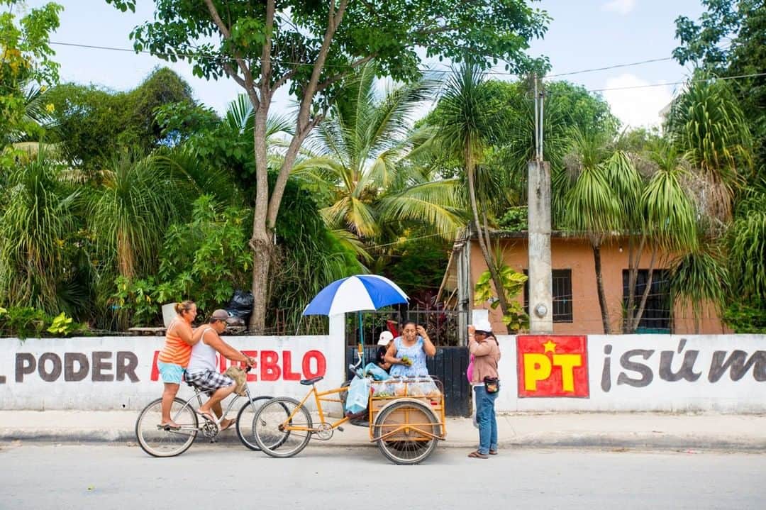 National Geographic Travelさんのインスタグラム写真 - (National Geographic TravelInstagram)「Photo by @emilypolar |  A local woman in Tulum checks the fruit and veg on her cart before pedaling through the heat while some patrons arrive at the right time to lighten her load. To see more of Mexico and beyond follow me @emilypolar #Mexico #Tulum #Streetfood」4月30日 13時02分 - natgeotravel