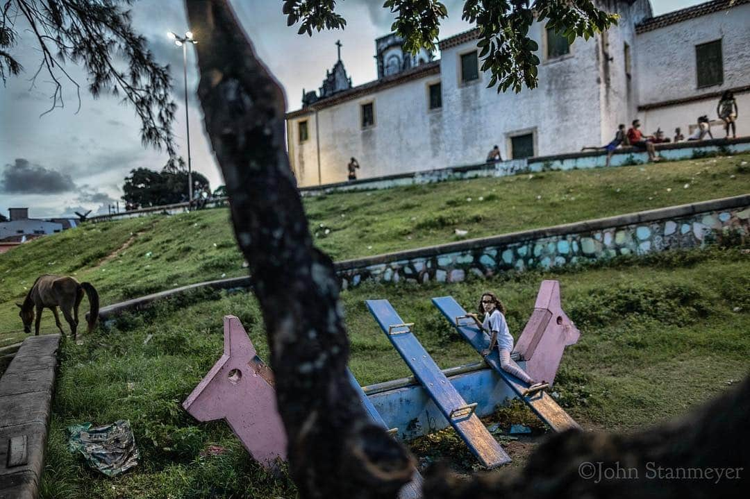 ジョン・スタンメイヤーさんのインスタグラム写真 - (ジョン・スタンメイヤーInstagram)「It was a pleasant, very hot first day in Olinda, spent mostly in this rather pretty 16th century town outside of Recife in northeast Brazil. This afternoon we arrived into the thickest heat I’ve felt in a while. Finally at sundown the heaviness began to calm, just enough for the locals to come out and play in this beautiful UNESCO village. Even a real horse appeared next a young girl playing alone on a two-horse headed seesaw. Everything moved slowly at this park beside a  Baroque style church. It was just too hot. ⠀⠀⠀⠀⠀⠀⠀⠀ Over a week already in Brazil, I’m here on the project, #LifeAsLived, for @natgeolearning @cengagelearning @rippleeffectimages. These photographs will be used on children’s school books all around the world. - @natgeolearning @cengage @natgeo @rippleaffectimages @natgeoimagecollection #brazil #olinda #playground #horse #seesaw #girlplaying #church #playing #children #unesco」5月1日 12時29分 - johnstanmeyer