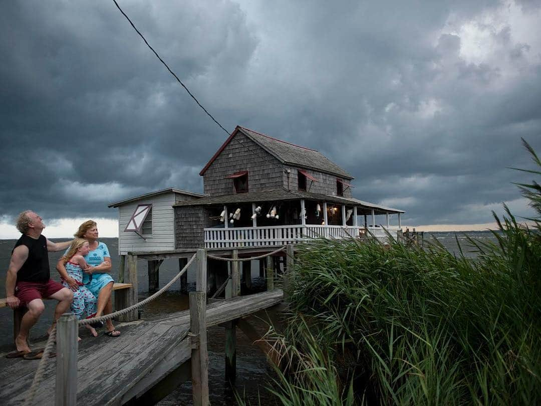 thephotosocietyさんのインスタグラム写真 - (thephotosocietyInstagram)「Photo by @davidalanharvey | We are often threatened by hurricanes here in the Outer Banks of N. Carolina. Statistics show us as target number one for these monster storms which originate in Africa before rolling into the Caribbean and then can veer up sweeping the entire eastern seaboard. Those of us who have chosen this barrier island, this sandbar, as home know we are taking our chances. These barrier islands are supposed to move with or without hurricanes or rising sea levels. My good neighbors Billy and Sandra Stinson were photographed by me for a NatGeo article on the outer banks. Ironically a summer storm cloud loomed in this published NatGeo Magazine picture,  yet none of us could imagine that just a few months later hurricane Irene would take away the Stinson summer home. Because I was already friends of the family from shooting and also a neighbor who had ridden out the storm, I was able to take the second image of the family grieving on the only piece of the house left after the soundside tidal wave took the house. Yet people want privacy in these moments. Diplomacy is a major part of people shooting. So I waded out in waist high water with a normal street camera moving very very slowly as not to disturb and hoping I did not step in a hole or trip or get hit by floating debris all of which were possible. Billy saw me out of the corner of his eye. If I had been any other news gatherer he would have been upset. Yet I knew I had to get this shot as part of the history of the outer banks and of course the Stinsons knew it too. Relationships matter.  To see the upcoming spring photo workshop at my home here in the Outer Banks see the link in my bio ( @davidalanharvey ) (May 19 - 25 / May 26 - Jun 1)」4月13日 3時31分 - thephotosociety