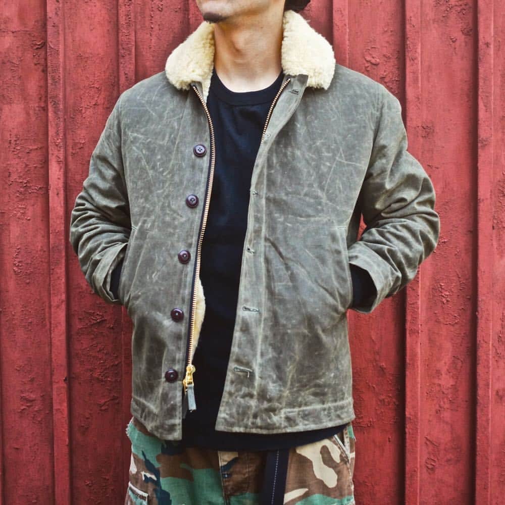 のインスタグラム：「N-1 Deck Jacket -Loden+Gold Mouton- . WESCOとのコラボでもお馴染みのDEHEN製“N-1 Deck Jacket”。 2014年の初登場から約5年の月日が経ち、これまでにカラーパターンも様々な組み合わせが発売されています。 . ヴィンテージアイテムの再生ではなく、“再起動”をコンセプトに今必要とされるモノを生み出していくことがDEHEN社の指針であるように、現在考えうる最高のマテリアルで製作したDEHEN渾身の“N-1 Deck Jacket”。 これまでN-1の弱点とも言われていた防水性を克服するべく用いられたのは、Martin Dyeing&Finishing Co.が作るMartexin®︎ 10.10ozのArmy Duckというドライワックスコットンです。 ワックスコットンと言ってもベタつかず、匂いもなくメンテナンス性に優れた素材となります。着込むほどに風合いが増し、アタリが付いて“自分だけの1着”に仕上がります。 また、N-1本来のライニングであるアルパカは毛が抜けてくるというデメリットを考慮し、襟から胴部分一面にはリアルムートンを使用し、高い防寒性と保温性を誇っています。 正しく『機能美』という言葉がふさわしい1着です。 . このモデルは、他Black+Black Mouton , Field Tan+Grey Mouton , Charcoal+Brown Moutonがラインナップ。 . #dehen #knitting #since1920 #99th #oregon #portland #madeinUSA #N1 #military #reboot #loden #gold #mouton #waxedcanvas」