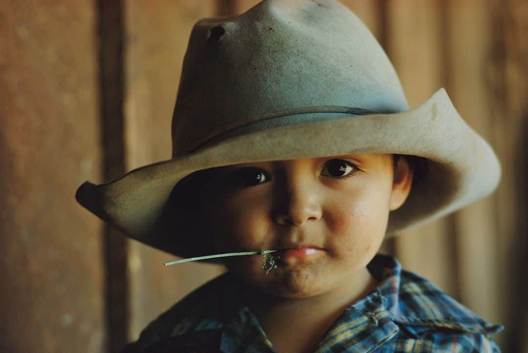 のインスタグラム：「Photo by William Albert Allard @williamalbertallard | This child wearing one of his papa’s hats is the son of John Hand, a rancher living in New Mexico back in 1971, when I was wandering the American West, taking photographs for the National Geographic book "The American Cowboy in Life and Legend," published in 1972. I don’t recall the boy’s name, but he was out in one of the barns where his father was shoeing a horse, and I found making portraits of the little boy more productive than watching the horse. This is a full, in-your-face portrait showing the boy's soft, smooth skin and dark, pool-like eyes, all accented by the piece of alfalfa clamped in his mouth. His father was a wonderful, highly respected rancher, and I’d like to think the little boy grew up to be the same, but I can’t say for sure. For more images of the American West and other assignments spanning a five-decade career, follow me @williamalbertallard」