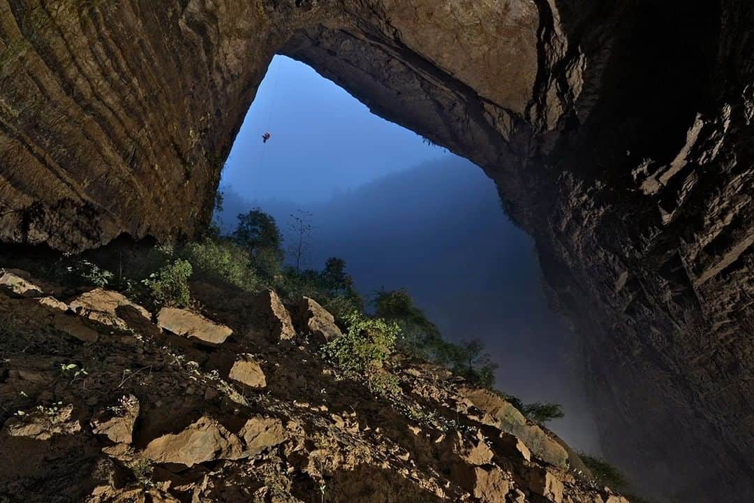 National Geographic Travelさんのインスタグラム写真 - (National Geographic TravelInstagram)「Photo by Robbie Shone @shonephoto | As night falls on the surface across Wulong County, China, a lonesome cave explorer ascends a rope out from the Niubizi Tian Keng, a collapsed cave chamber that is now open to daylight. Clouds rise from the saturated vegetation on the floor of this mighty Tian Keng. This giant portal will soon be shrouded in total darkness and left to its natural state.」5月15日 9時41分 - natgeotravel