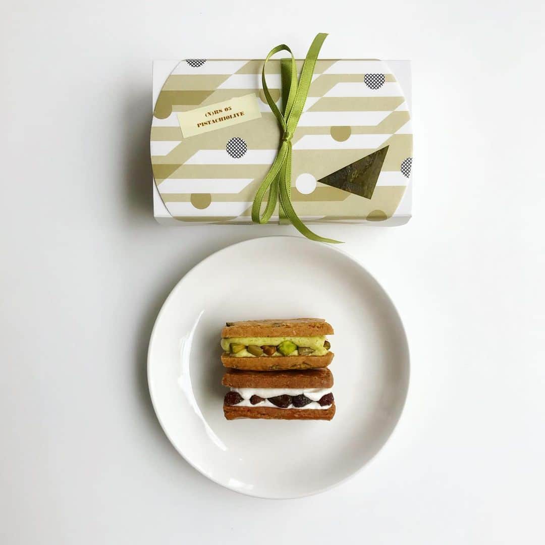 のインスタグラム：「《5/22 20:00予約開始》(NO) RAISIN SANDWICH 新味 🍃🕊PISTACHIOLIVE🕊🍃できました～。香り高いピスタチオクリームに香ばしいローストピスタチオをサンドして、オリーブの塩気とほのかなタイムの高揚感をアクセントに。晴れやか＆リッチな新緑フレーバーは、ワインともしっかり握手🤝✨浮き足立つようなおいしさに仕上がったよ〜どうぞよろしくお願いします！🕊✨ ——————— -(N)RS 05《PISTACHIOLIVE》 6個入 ¥2,300(税込) -お受け渡し日: 5/26(日)16:00-18:00 @path_restaurant (東京都渋谷区富ヶ谷1-44-2) -お菓子は事前予約販売制です -5/22(水)20:00よりhttps://noraisinsandwich.stores.jp/ にて予約販売を開始します -購入はお一人様1つまででお願いいたします -商品郵送のご対応はできません -商品の詳細は https://noraisinsandwich.stores.jp/ をご確認ください -お問い合わせ先 noraisinsandwich@gmail.com 🕊🍃 企画 @sakikohirano 製菓 @yuichi.goto 意匠 @mina_tabei @noraisinsandwich #noraisinsandwich」