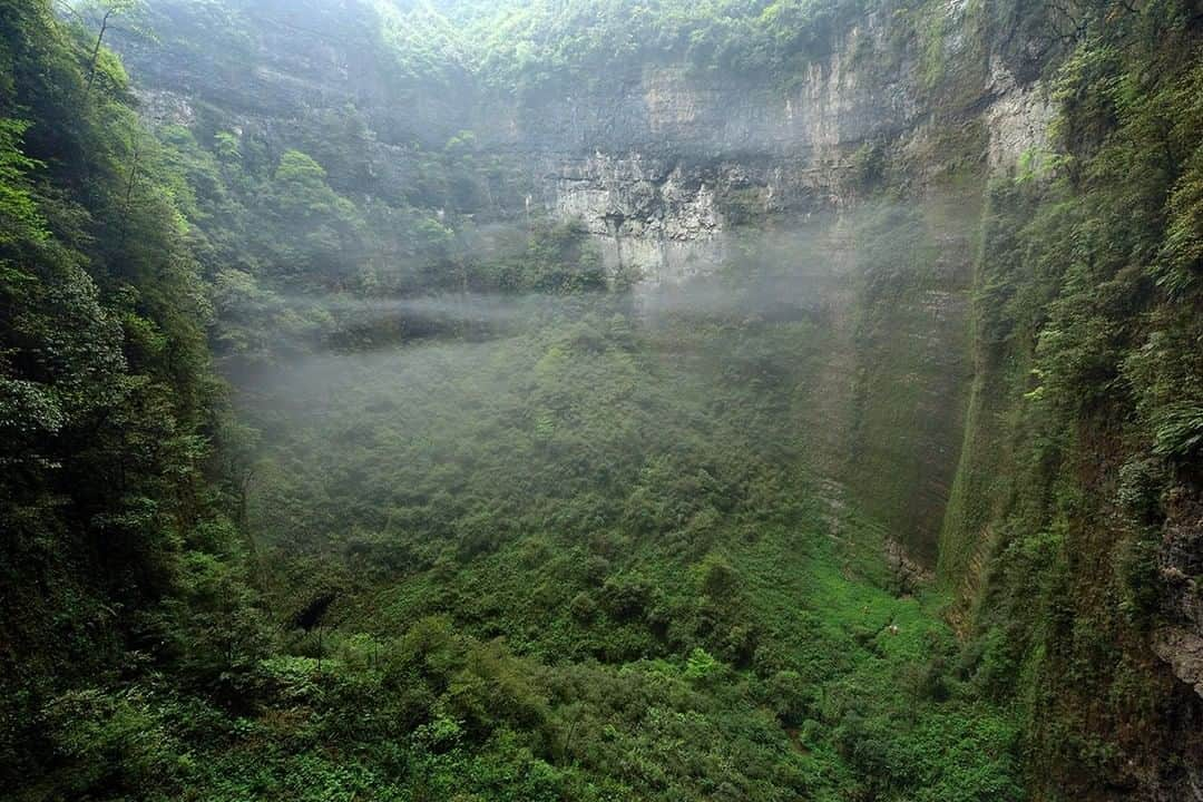 National Geographic Travelさんのインスタグラム写真 - (National Geographic TravelInstagram)「Photo by Robbie Shone @shonephoto | In a small clearing surrounded by trees and thick vegetation, three tiny explorers admire the scale of the Niubizi Tian Keng in Wulong, China. In such a space, the obvious question to ask by any cave explorer is how  big the cave chamber must have been before the roof collapsed in opening it up to the daylight outside. Hidden from view, this lost world now contains it's own unique ecosystem thriving, secluded in paradise. Thin wisps of clouds gather and gently rise up following a heavy downpour of rain.」5月19日 22時04分 - natgeotravel