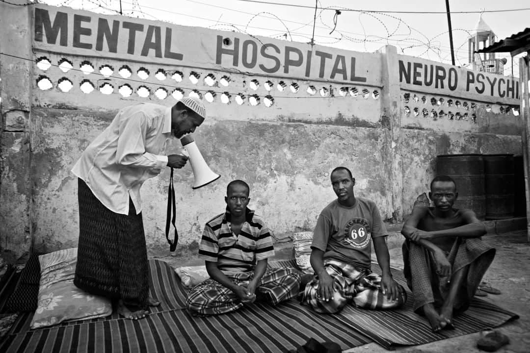 のインスタグラム：「Photo by Robin Hammond @Hammond_Robin | I am not a war photographer, but several times while documenting mental health in Africa I found myself in the middle of a conflict. When I arrived in Mogadishu in 2011, the front line ran down one of the main streets. This photo is from a former psychiatric hospital close to the fighting. The foreign, nongovernmental organization running it had left. A Muslim cleric took over, and here he recites verses of the Quran through a blowhorn, in an attempt to heal patients. The World Health Organisation @WHO has said 1 in 3 Somalis live with a mental health condition. After decades of war, famine, and displacement this can hardly be a surprise. May is Mental Health Awareness Month. Photographers can raise awareness, but I wonder how useful that is if it does not lead to action. On the campaign website www.onedayinmyworld.com you can read about my own struggle with this question. To see more from the project (and to find a link to that story) follow @onedayinmyworld」