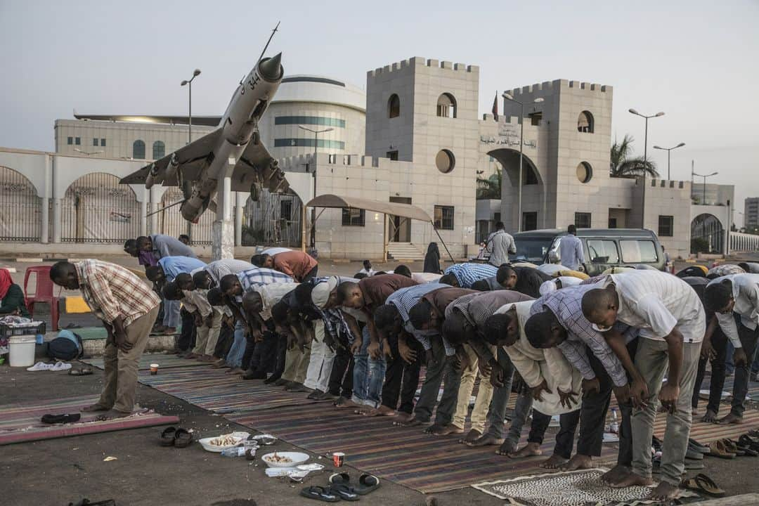 ルモンドさんのインスタグラム写真 - (ルモンドInstagram)「Au cœur de Khartoum, capitale du Soudan, l’aéroport est bordé sur sa partie nord par tout un ensemble de bâtiments militaires. Sa vaste enceinte comprend aussi une résidence présidentielle, et, un peu plus bas, le siège des services de renseignement soudanais. Devant les portes entre le Nil et l’état-major de l’armée de l’air et de celui de la marine, se tient le sit-in, cette cité de la révolution qui a poussé avec ses tentes et ses manifestants. Dans cette ville si grande, si étalée, c’est dans ce tout petit coin que se joue la situation politique du pays. Après le renversement d’Omar Al-Bachir, le 11 avril, le Soudan est le théâtre, dans une tension croissante, de difficultés à trouver une solution à la transition. Une grève générale de deux jours devrait débuter dans ce climat, mardi 28 mai. >> Retrouvez l'actualité du continent Africain sur notre compte : @lemondeafrique - 1 : Au sein du sit-in, dans le centre de la capitale, Khartoum, le 25 mai. 2 : Les centaines de manifestants prennent l’iftar chaque jour sur place. 3 : Installés devant les bâtiments du ministère de l’aviation, de la marine et de la défense, les manifestants prient au coucher du soleil. - Photos : Laurent Van der Stockt (@laurentvanderstockt) #PourLeMonde - #Soudan #SudanUprising」5月28日 18時10分 - lemondefr