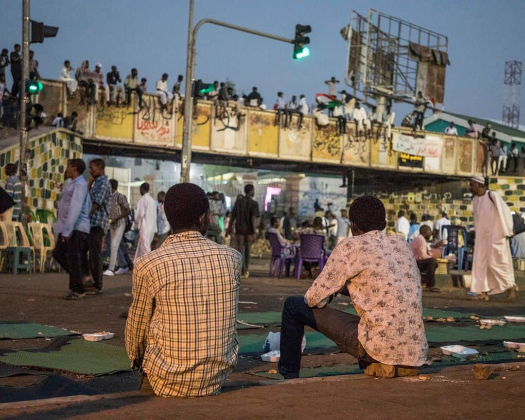 ルモンドさんのインスタグラム写真 - (ルモンドInstagram)「Khartoum 31 mai. Les ruraux qui envahissent les rues du centre sont là pour signifier une possible divergence du programme. Un test. Collectivement, ils ressemblent un peu au visage de la contre-révolution : on les a convoyés pour leur faire dire à quel point ils croient plus au pouvoir des militaires, à la prédominance du respect de l’islam qu’à toute autre considération présidant à l’organisation de la société soudanaise. Et qu’ils se contrefichent de la série de choses qui se discutent dans les rues de Khartoum nuit et jour, à moins de quinze minutes de marche.  Alors que géographiquement, tout se déroule dans un mouchoir de poche, on ne saurait être plus éloigné. Alors qu’au sit-in, festival de l’élan démocratique au Soudan, le débat et la fête continuent devant le quartier général de l’armée, un autre pays semble avoir envahi la rue pour un sit-in bis, mais express aux abords de l’avenue Al Qasr, l’avenue du palais, qui débouche effectivement à la présidence, ou plus exactement à l’entrée des deux présidences conjointes qui trônent le long du Nil : l’ancienne, toute blanche datant de la période coloniale, et l’autre, toute de marbre et de pierre sculptés, offerte par la Chine. >> L’actualité du continent africain est aussi sur notre compte @lemondeafrique<< - 1 et 2 : Après les deux jours de grève organisée par les dirigeants du mouvement civil de contestation, ceux ci continuent à occuper le sit-in aux abords du quartier général de l'armée. 31 mai.  3 et 4: En fin de journée, une manifestation en faveur du conseil des militaires a réuni plusieurs centaines de personnes amenées en bus au centre-ville.  Des slogans en faveur de la charia en vigueur étaient chantés et des portraits de Hemeti et de Abdel Fattah al-Burhane, les chefs du conseil militaire, étaient brandis.  Photo : @laurentvanderstockt #PourLeMonde — #Sudan #Uprising」6月1日 14時12分 - lemondefr