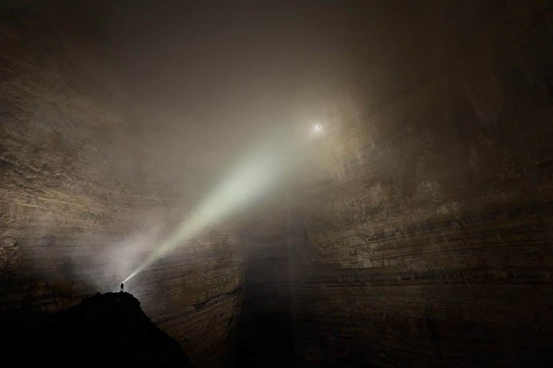 National Geographic Travelさんのインスタグラム写真 - (National Geographic TravelInstagram)「Photo by Robbie Shone @shonephoto | The limestone in this region of China is so strong, it can withstand such giant voids like Cloud Ladder Hall. Eventually though, over time, the weight of rock above will become too great and it will collapse, forming a giant sinkhole or Tian Keng, a huge hole open to the surface. This gigantic cave that has never seen the light of day is a tough photography target under clear conditions. But this one posed an extra challenge: it's so large and so isolated that it has its own weather – including clouds. Weather makes its way in, but it can't  make its way out. For this photograph, I had three accomplices: one standing out of frame with a large single-use flash bulb, one standing on the rock to the left shining her headlamp at the cave wall, and a third dangling from a rope hundreds of metres away. Although the shutter was open for only 30 seconds, the whole operation took four hours, with the team communicating via walkie-talkie because the echoes made shouting unworkable.」6月3日 4時11分 - natgeotravel
