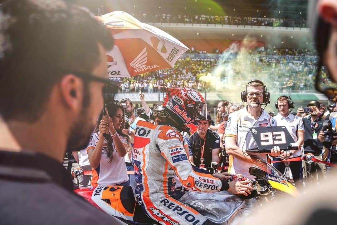 レプソル・ホンダのインスタグラム：「HRC Photographer @cormacgp: ⠀⠀⠀⠀⠀⠀⠀⠀⠀ The grid is always a hectic place, but the grid at Mugello is a little bit 'extra', compared with the rest. I like this photograph because it conveys that atmosphere, that controlled chaos that Italy & Mugello is so famous for. Yellow flares being let off everywhere, including in the background here, while Marc Márquez tries to find his own moment of peace and concentration before the start of the MotoGP race. The hustle and bustle is evident here, engineers with laptops, grid girls with umbrellas, photographers with their cameras and Marc's assistant Jose in the foreground, all there doing individual jobs, all adding to that controlled chaos. A few minutes later and the world's best riders would head towards turn one for an intense and very Mugello-esc MotoGP race. ⠀⠀⠀⠀⠀⠀⠀⠀⠀ ISO 50, 24mm, f/2.8, 1/400 sec」