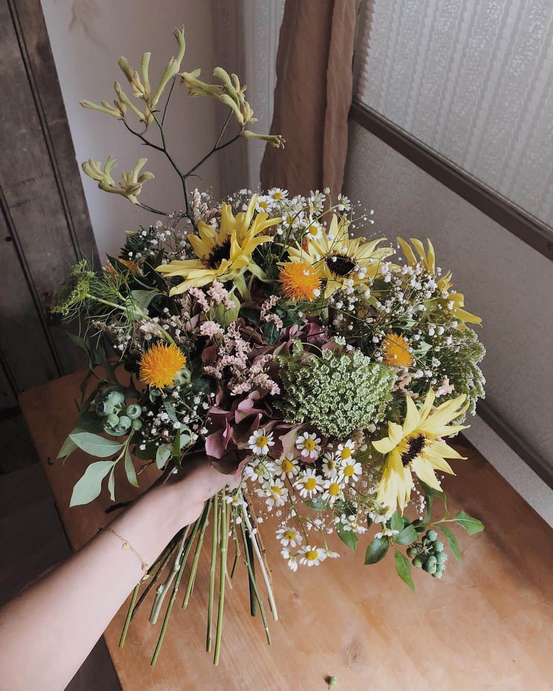 目見田早弥子のインスタグラム：「| bouquet 𓆸  前回のマロンのレッスンはまたまたブーケ💐 ブーケはやればやるほど感覚が掴めてくるし スパイラルが綺麗にハマっていく感じが好き！ 今回はヴィンテージカラーのアジサイを土台にして 空間をカスミソウやシネンシスで埋め、 ヒマワリをブーケの顔に。 鮮やかなオレンジで丸みのある紅花をポイント使いし、 リズミカルなマトリカリアや レースフラワーで全体に動きを。 カンガルーポーでアクセントをつけ、 最後はブルーベリーでバインディングポイントを カバーして完成です⚐ 今回のレッスンでは大きなアジサイに花をさしていって ひとつのブーケにするのが斬新で面白かった！ アレンジメントも楽しいけど 生花のブーケが一番やり甲斐を感じる！ 正解はないけど この方が雰囲気キマるなぁっていうのはあって、 お教室ではそれが先生と共感できたときに うわぁ、ちゃんと学べてる、嬉しい！ って思うなあ😂🌸 @marronpapier_jp」