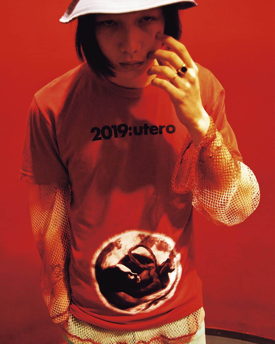 のインスタグラム：「胸もとの「2019:uteri（＝2019年の子宮）」のロゴ通り、お腹のなかにいる赤ちゃんのエコー写真を腹部にプリントした「HOMME BOY」の真っ赤なカラーTシャツ。ムラ染めされたフィッシュネット状のカットソーを下に重ねたどこかパンクな世界観の着こなしに、対照的なカラーのボトムやハットでカラーリングを意識。  july issue Summer manifesto  model @y.slug_  t-shirt,top @hommeboyco bottoms @martinasbjorn hat @allege_official 《NYLON guys JAPAN Instagram ▶︎ @nylonguysjapan 》 #nylonjapan #nylonguysjapan #nylonjp #summermanifesto #tshirt #fashion #culture #caelumjp」