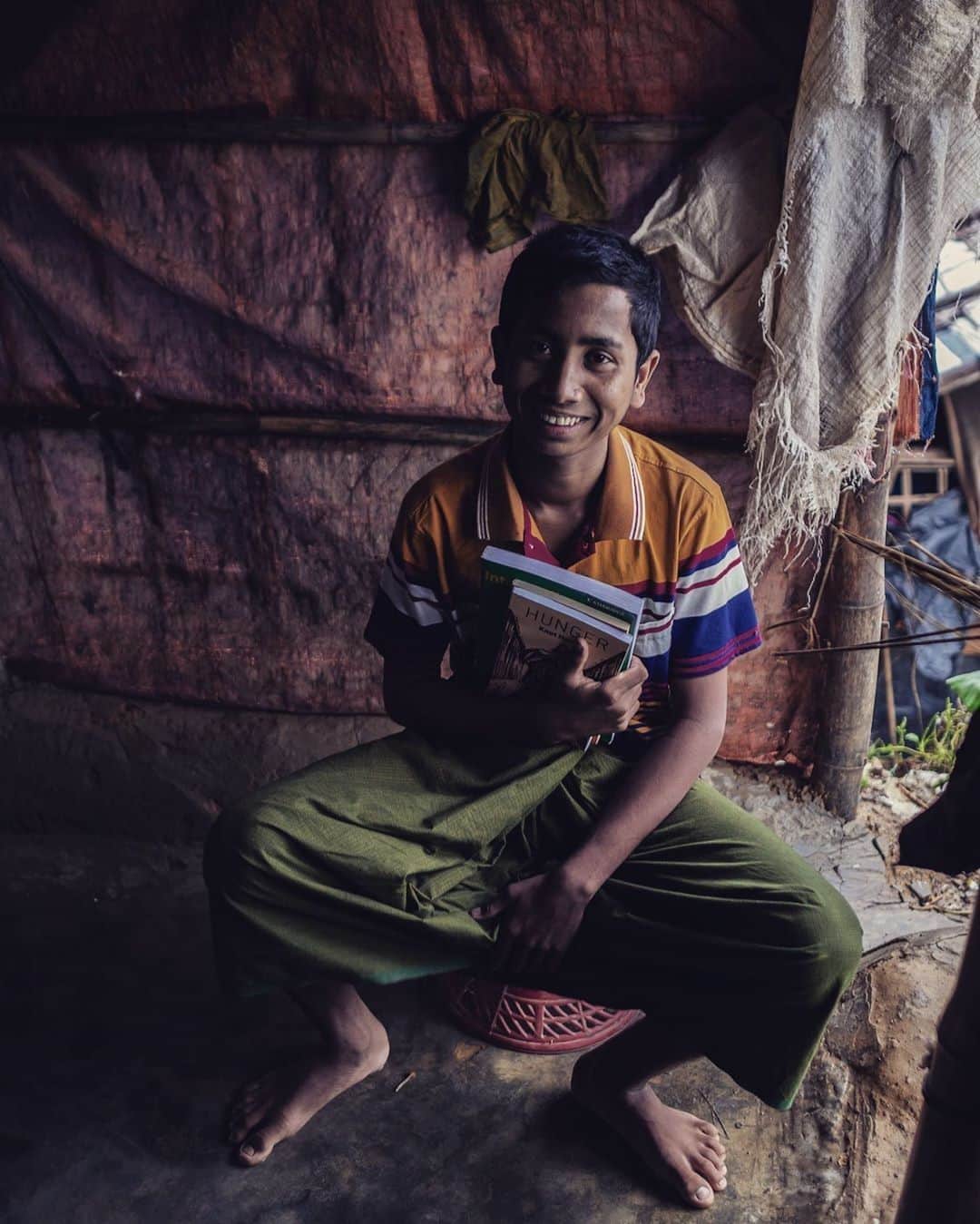 unicefさんのインスタグラム写真 - (unicefInstagram)「With limited learning opportunities in the camps, Rohingya refugee children are taking education into their own hands. Mohammad's story, shared by @thomasnybophoto, will inspire you. 👇📚 . . . #regram Two weeks ago while walking through heavy mud on a rainy day in the world’s largest refugee camp, I heard a determined, quiet voice reading English. The story was about a picnic in the park. I followed the voice and found a teenage Rohingya boy named Mohammad sitting in the doorway of his family’s plastic and bamboo shelter. The book was called “Reader 5, Grade 6” and Mohammad had carried it with him from Myanmar when his village was attacked by soldiers. He reads it constantly because in the camp he has nothing but time; and he spends that time, four or five hours a day, practicing his English, sometimes with a local tutor, sometimes by himself in the doorway with his book. I got back to my hotel that night and told my colleagues about this remarkable boy who we needed to buy some books. @laladumonde2018 showed up a few days later with a wrapped package containing three books: a more-advanced English text book; Paulo Coelho’s The Alchemist; and Hunger by Knut Hamsun. Today, on my last day in the camp, I walked back through the mud to Mohammad’s tent and told him that I believed in him, and that he inspires me. “This is for you,” I told him, handing him the package. Mohammad took out each book and held it, and ran his hand along the front cover and the spine, and then he turned to me. “Thank you,” he said. I asked him if I could take his picture with his books. Mohammad put on his best shirt, sat down with his new books, and he smiled. #rohingya #refugees #bangladesh #books #paulocoelho #hunger #knuthamsun」7月14日 21時55分 - unicef