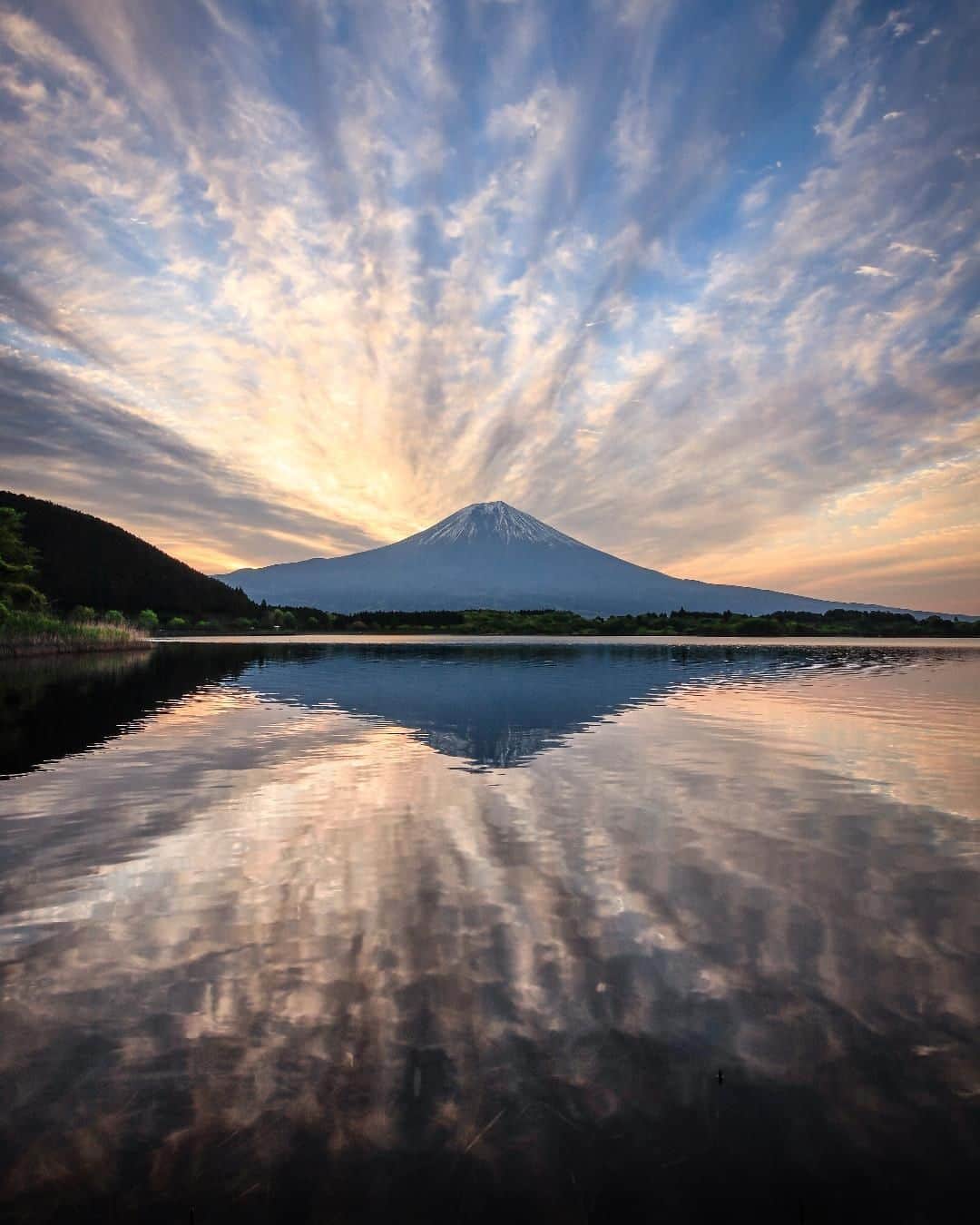 Canon Asiaのインスタグラム：「Imagine being greeted with such a breathtaking sight early in the morning! This majestic shot of Mount Fuji 🗻, wispy clouds ☁️ and the waters 🌊 of Lake Tanuki by @hashimuki on the Canon EOS R has got us in awe. • Leading lines can be especially useful in landscape shots 🖼️ with multiple elements! Use them to draw attention to your main subject, like how the linear clouds in the sky and their shimmering reflection ✨ in the water instantly highlight the grand peak of Mount Fuji as a strong focal point. • 📷 Image by @hashimuki shot using the Canon EOS R | f/18 | 1/15s | ISO 100 | 15mm  Want your photos to be featured too? Tag them with #canonasia !  #canonasia #photography #mountfuji #japan #japan_of_insta #japan_night_view #landscapephotography #reflection #reflectiongrams」