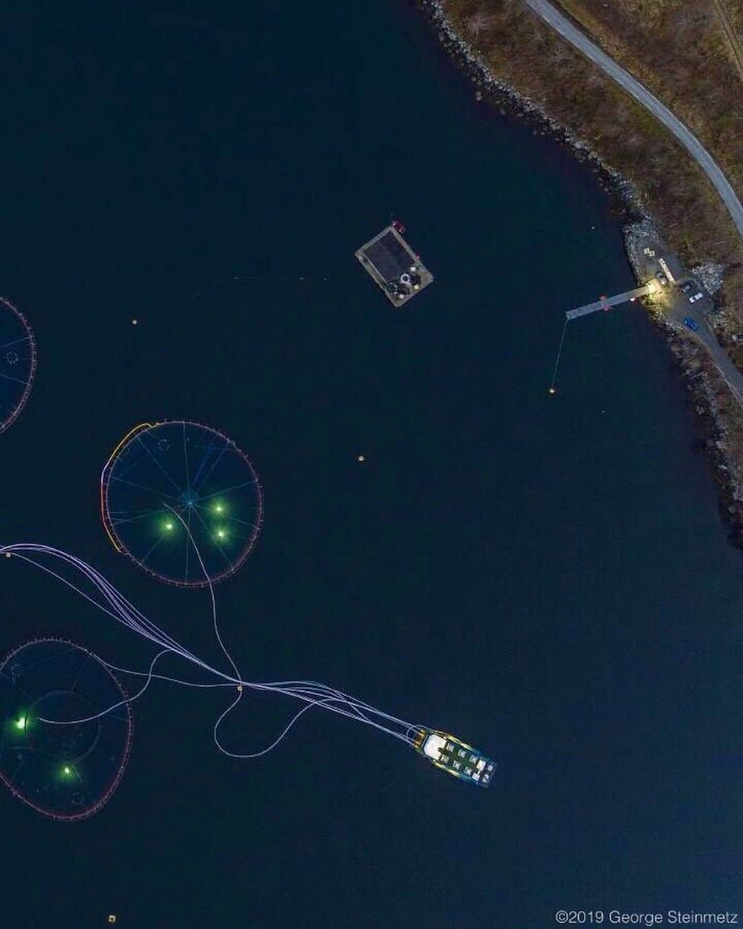 ナショナルジオグラフィックさんのインスタグラム写真 - (ナショナルジオグラフィックInstagram)「Photo by George Steinmetz @geosteinmetz | About 1.2 million Atlantic salmon swim in the pens in Hjorrund Fjord, Norway. They are fed pellets of fish meal, fish oil, and soybeans via pneumatic tubes from the barge (at left). The lights come from underwater video cameras that monitor whether all the food sprayed into the pens is being eaten. To learn more about where our food comes from, follow @FeedThePlanet.」7月16日 6時42分 - natgeo