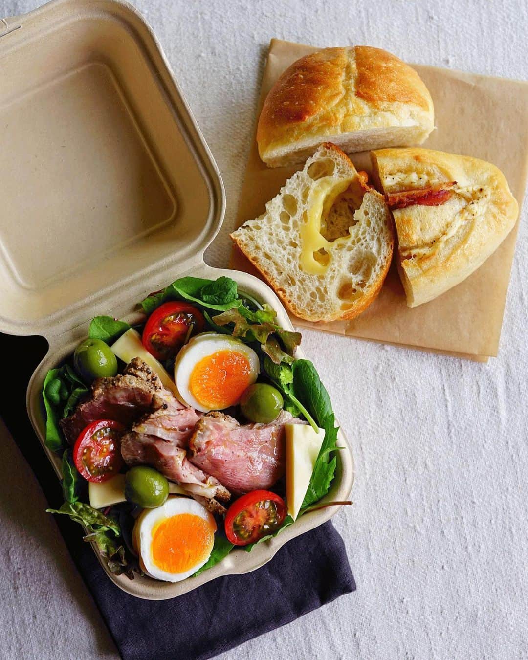 Ryoko Yunokiのインスタグラム：「+ + + Bread and salad bento/パンとサラダのお弁当 . *some bread *Green salad, topped with roasted pork, hard-boiled egg, baby tomato, cheese and green olives, seasoned with salt/pepper and drizzled olive oil . *パン *グリーンサラダ。ローストポーク、茹で卵、プチトマト、チーズ、グリーンオリーブ。味付けは塩胡椒とオリーブオイル。 + + + #bento #お弁当 #丸の内弁当 #f52grams #紙パック弁当」