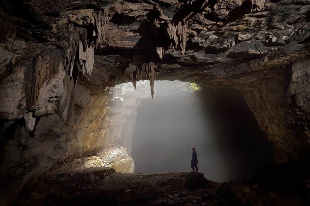 National Geographic Travelさんのインスタグラム写真 - (National Geographic TravelInstagram)「Photo by Robbie Shone @shonephoto | In rural China, the local villagers are always more than happy to help us search for caves. They have worked the land all their lives and often can guide us straight to cave entrances. Pictured here inside Dong Wan Dong, one farmer admires this spectacular giant skylight bursting in from above where a wonderful ray of sunshine illuminates the darkness. I remember he was very keen to lead us through to this spot where the skylight shaft was, but went no further as the cave dropped away down a giant slope of rocks and boulders. He stayed behind and let us go on ahead to explore the blackness.」7月8日 19時01分 - natgeotravel